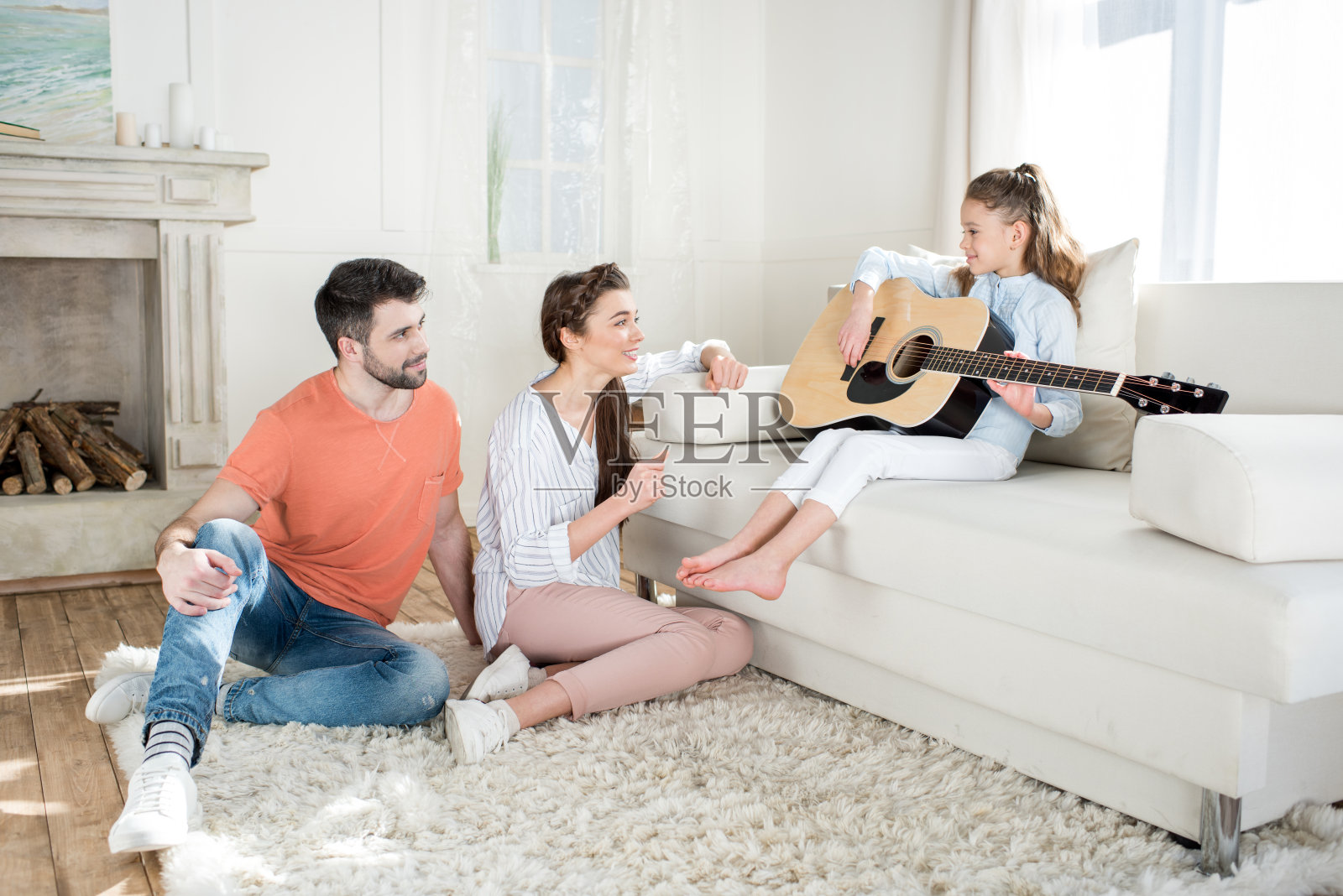 快乐的父母坐在地毯上，看着女儿弹吉他照片摄影图片