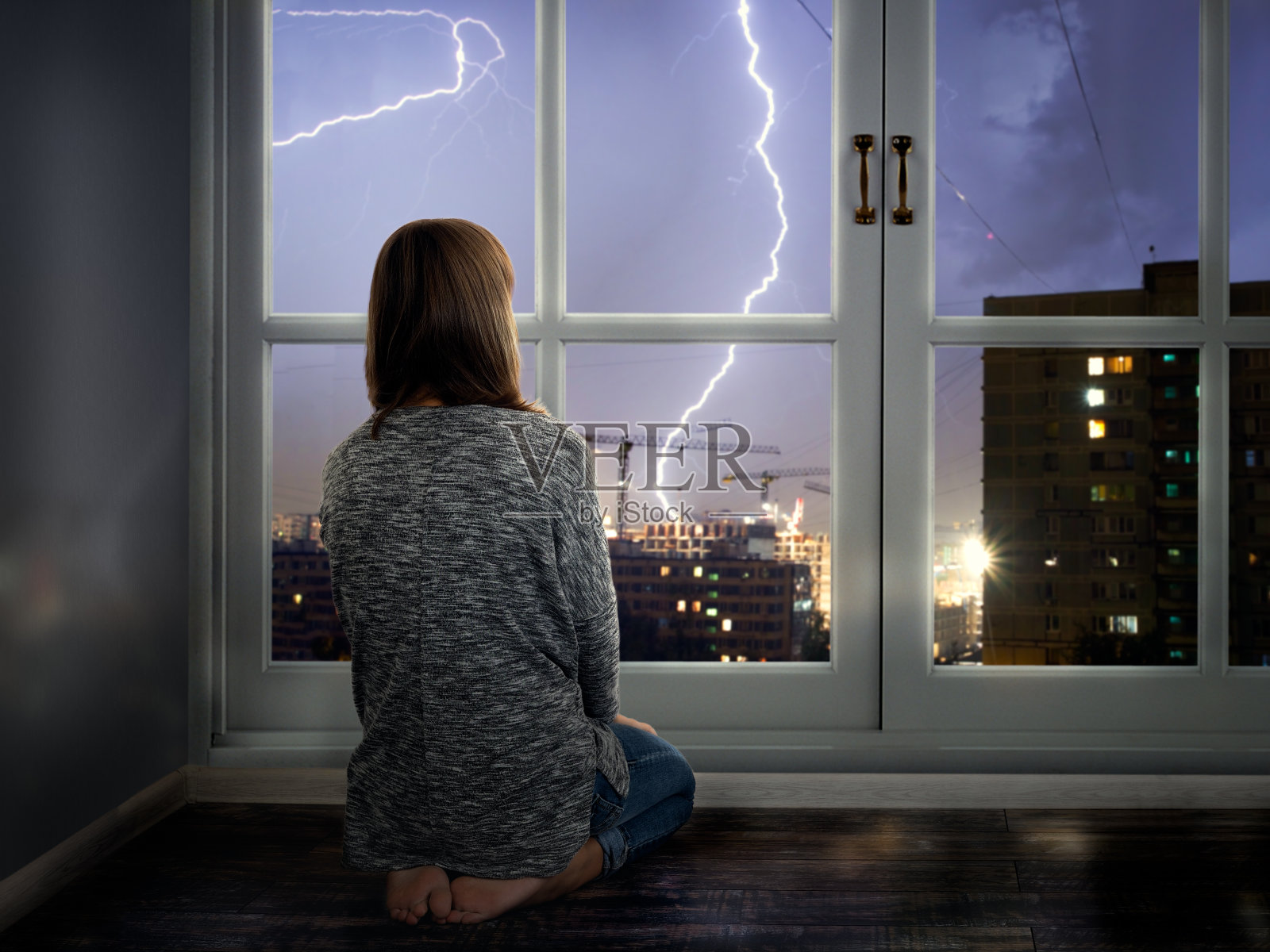女孩透过窗户看闪电。城市里的雷雨照片摄影图片