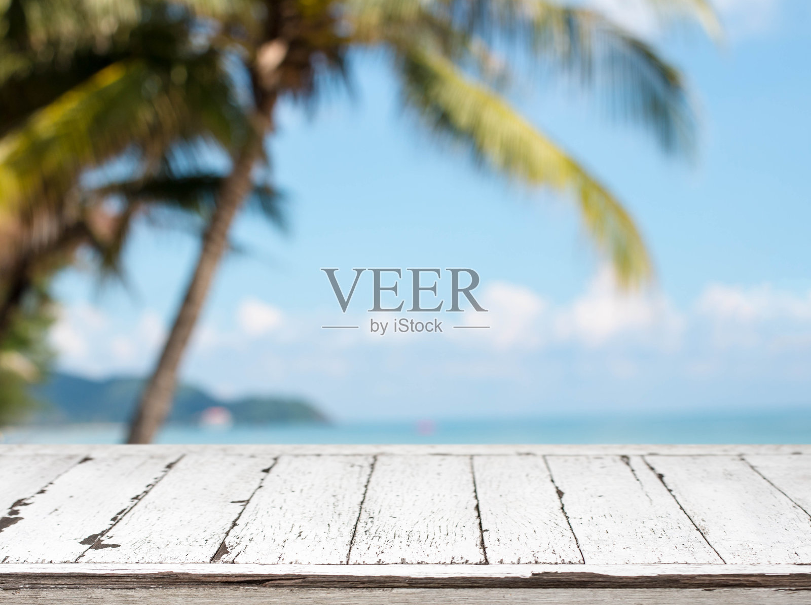 木质桌面和模糊的夏日海滩椰子树和蓝天背景。-可以用于展示或蒙太奇您的产品。照片摄影图片