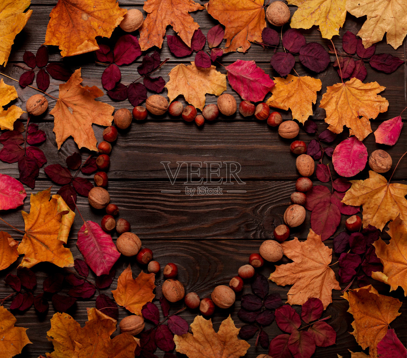 平面布局框架的形式，一个心的秋天深红色和黄色的叶子，榛子和核桃在黑暗的木制背景。照片摄影图片
