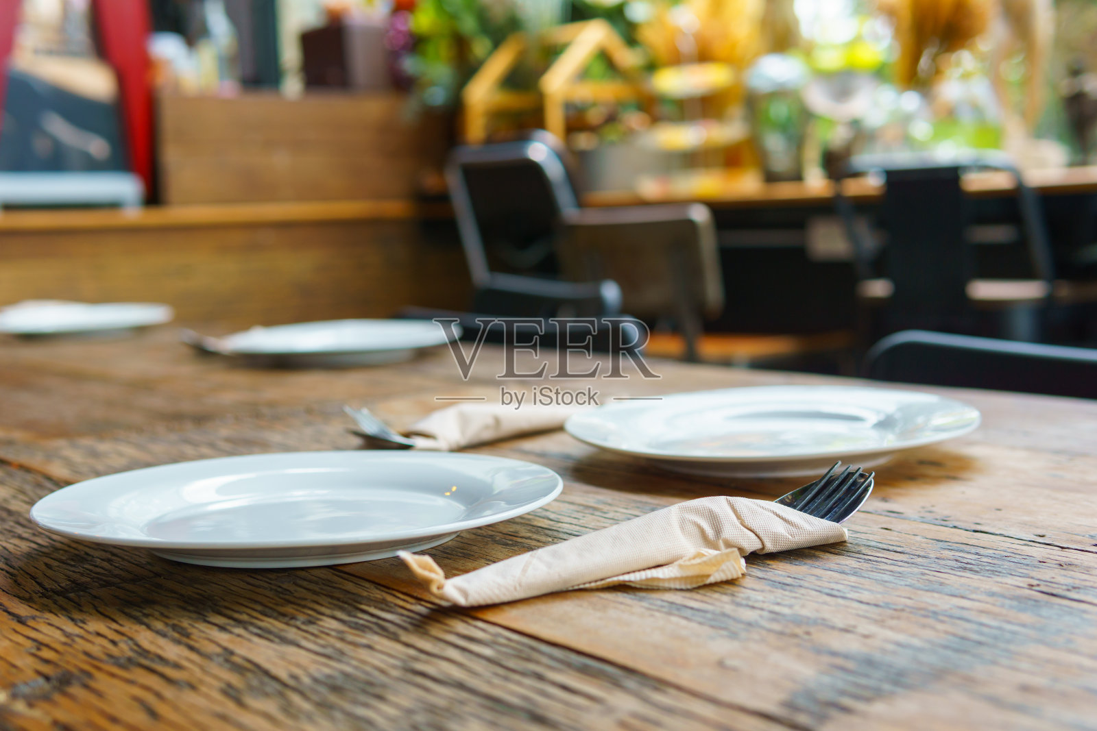 侧视图。三个白色的空盘子和刀叉放在古老的木桌上，模糊的咖啡馆背景。照片摄影图片