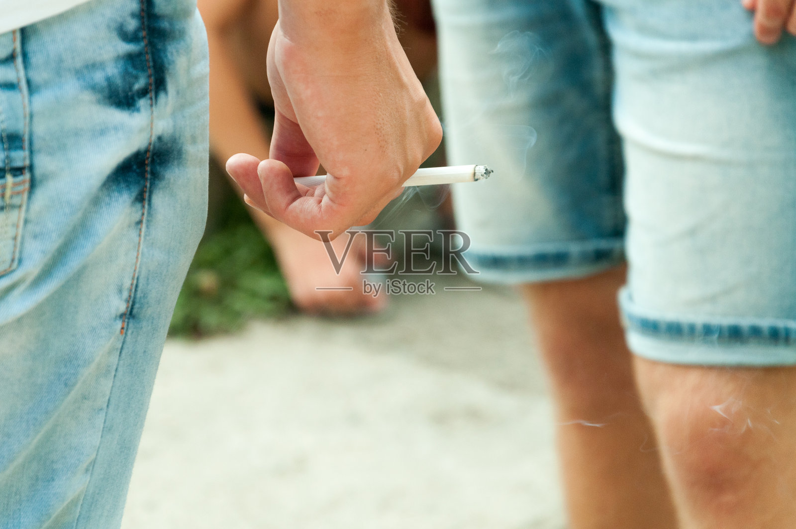 一个年轻人手拿香烟，站在人群中的街道上。照片摄影图片