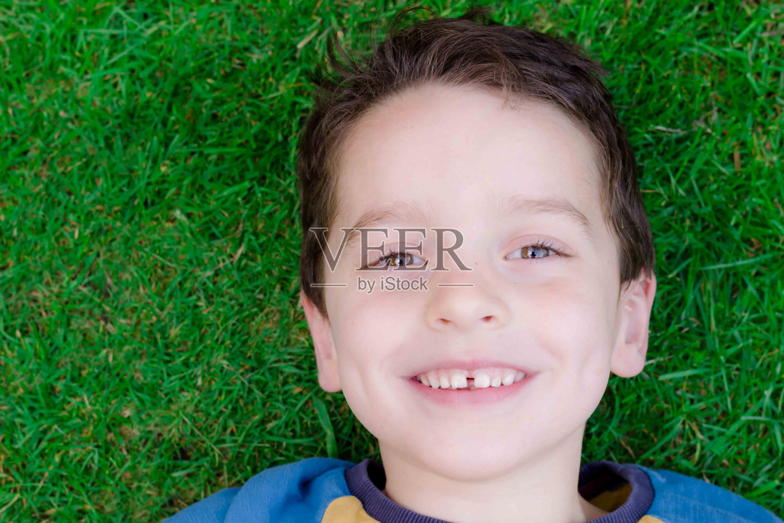 5岁左右的小男孩躺在草地上，面带微笑照片摄影图片