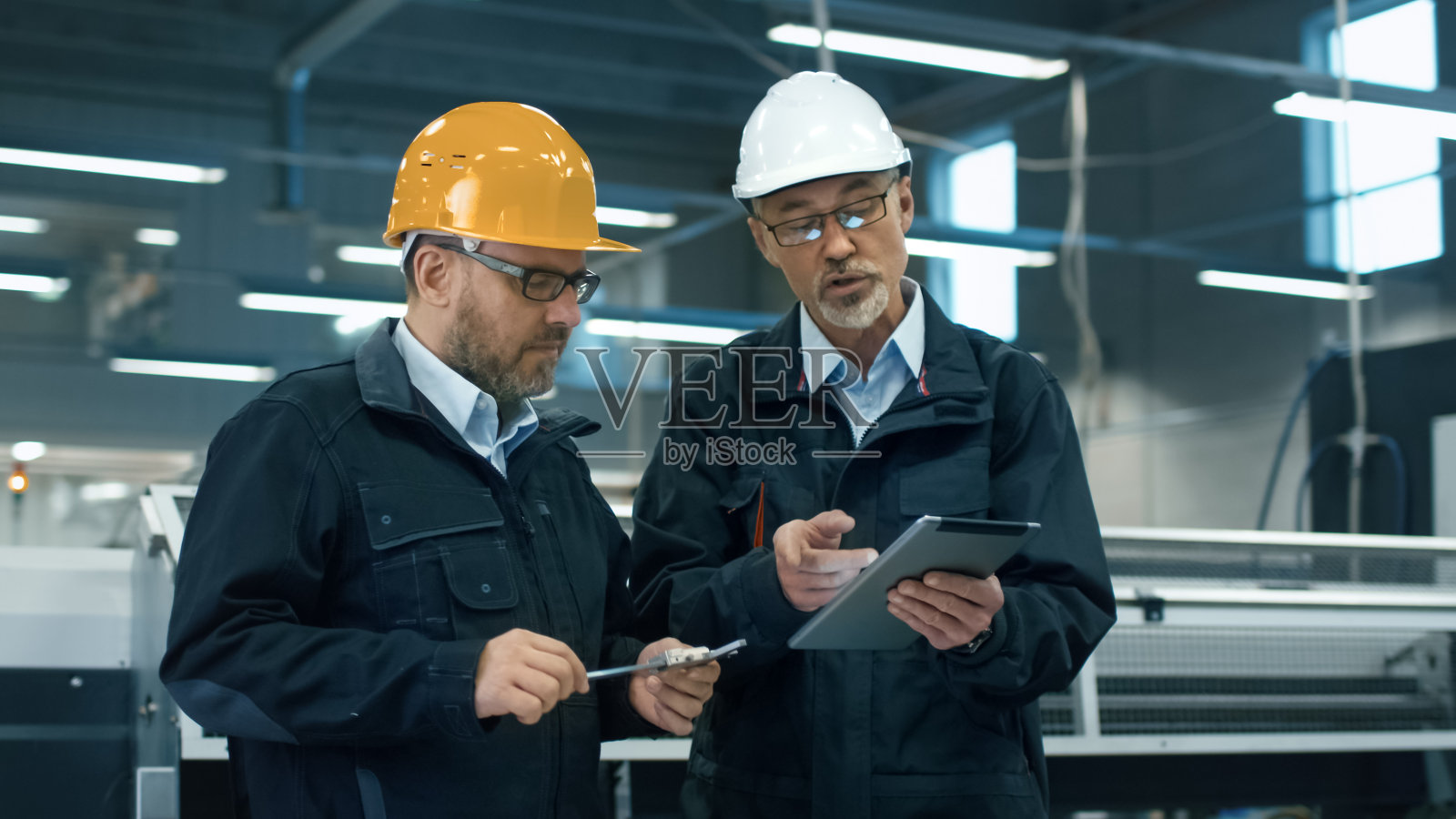 站在工厂里，两位工程师戴着安全帽在平板电脑上讨论信息。照片摄影图片