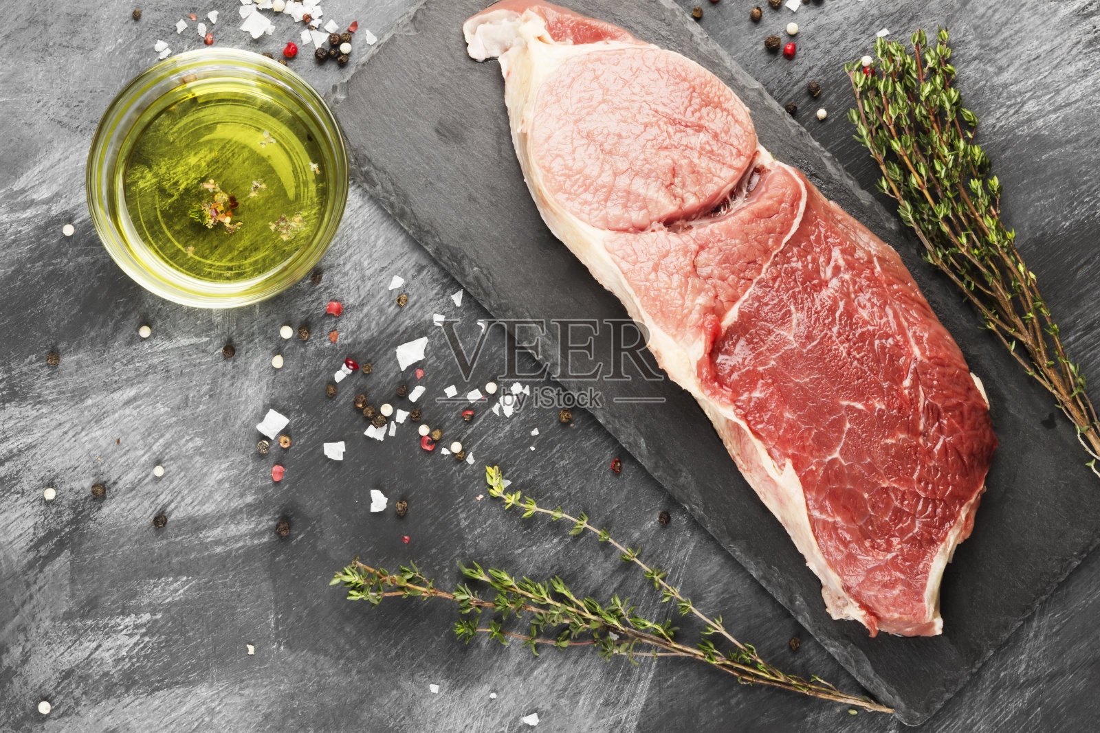 一块生牛肉放在一块石板上，配上胡椒、橄榄油和百里香，背景是黑色的。俯视图，复制空间。食品的背景照片摄影图片