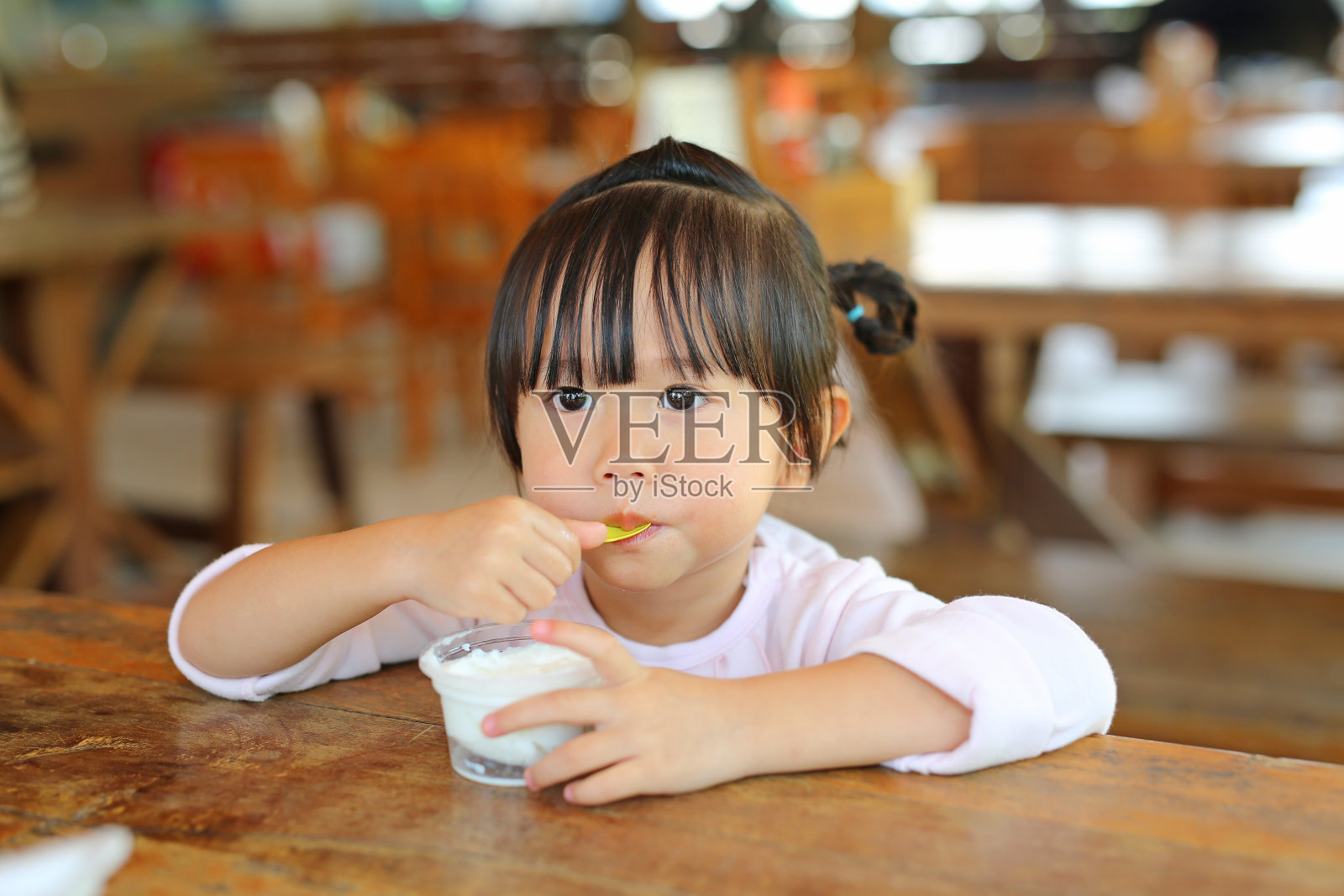 一个亚洲小女孩在吃杯里自制的冰淇淋。照片摄影图片
