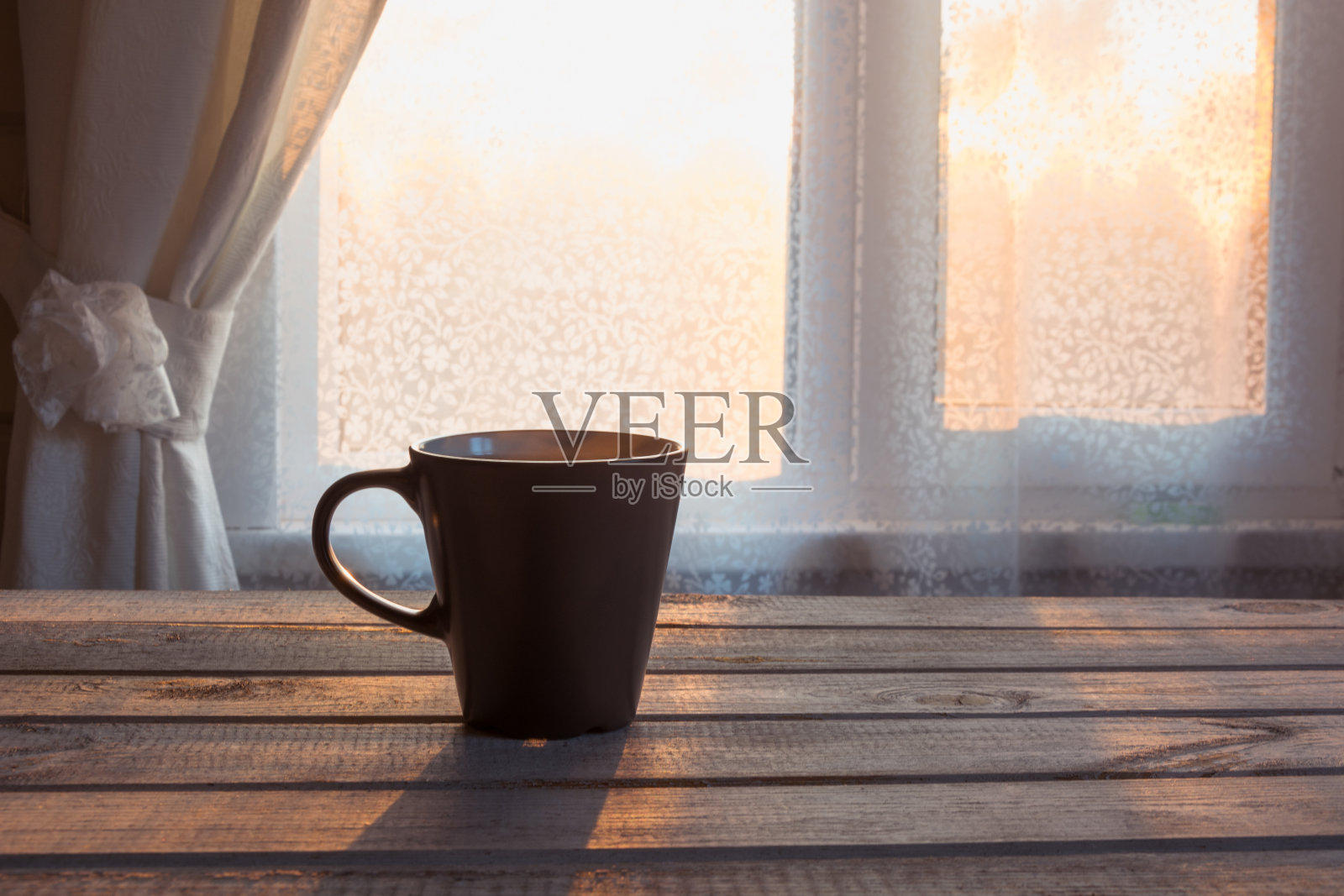 一杯黑咖啡和一个花边在窗前的木制背景。照片摄影图片