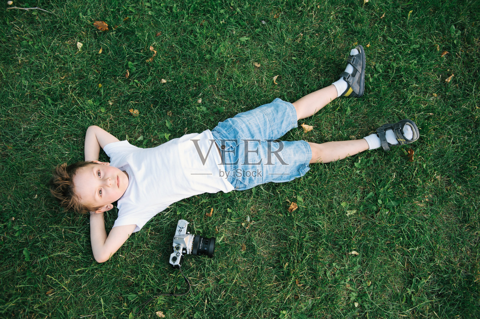 英俊的小男孩躺在绿色的草地上，旁边是落叶胶卷照片摄影图片