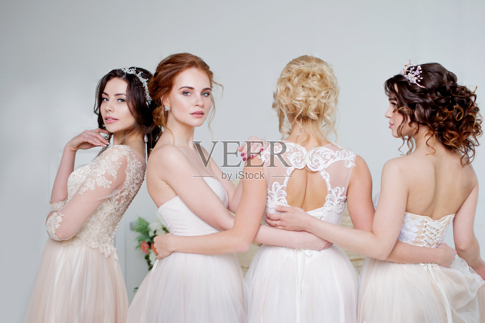 新娘在婚礼沙龙。四个美丽的女孩相互拥抱着。背部，特写蕾丝裙照片摄影图片