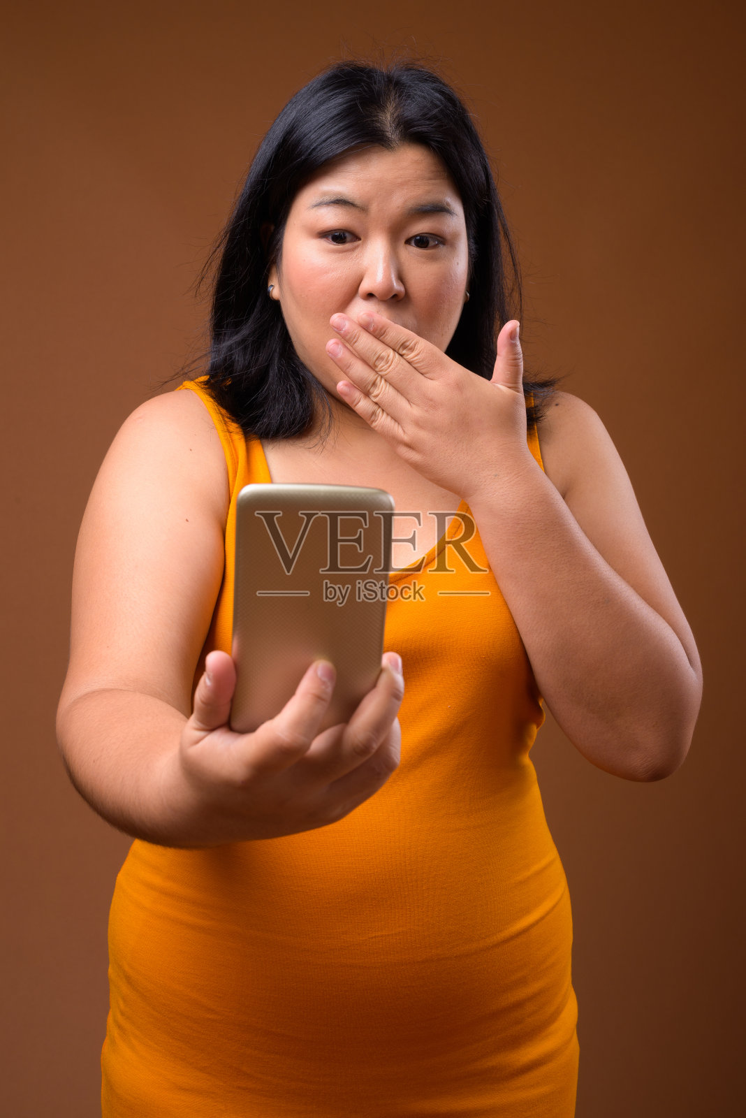 摄影棚拍摄的超重的亚洲妇女穿着黄色的橙色衣服，以彩色的背景照片摄影图片