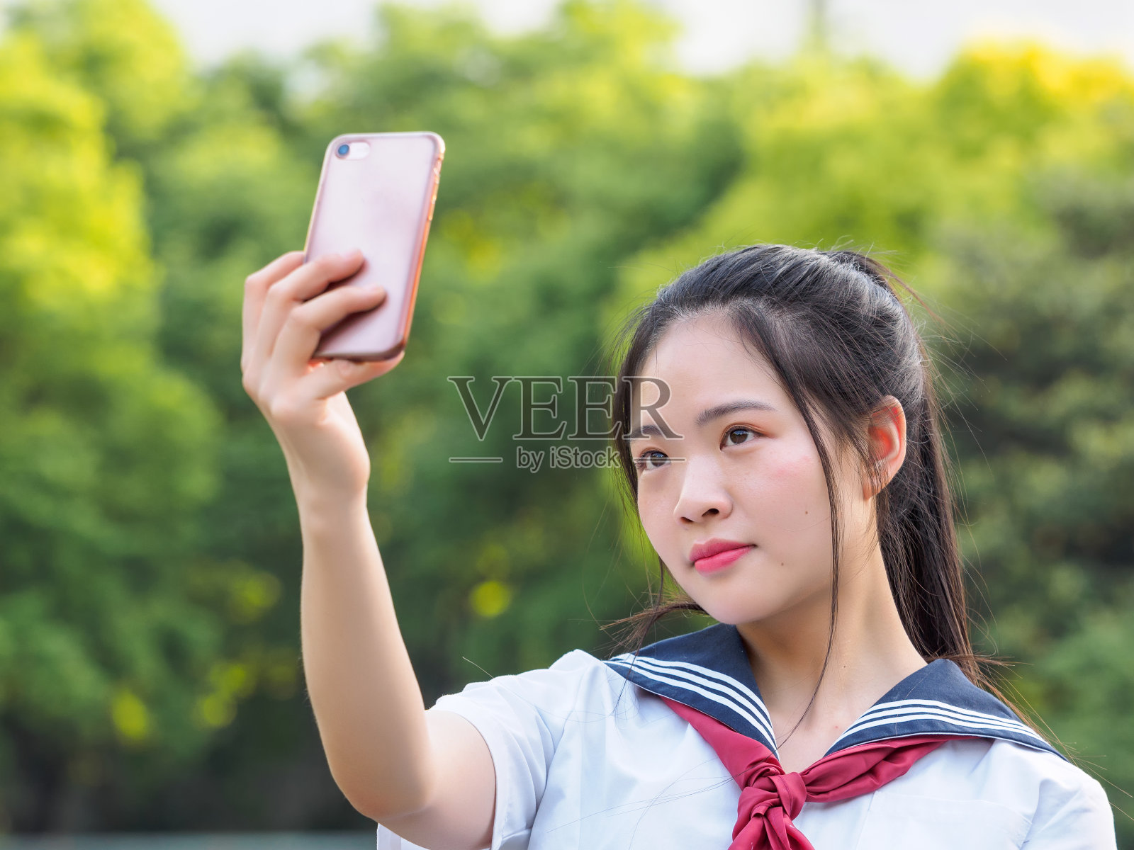中国女学生穿着校服，用智能手机自拍。照片摄影图片