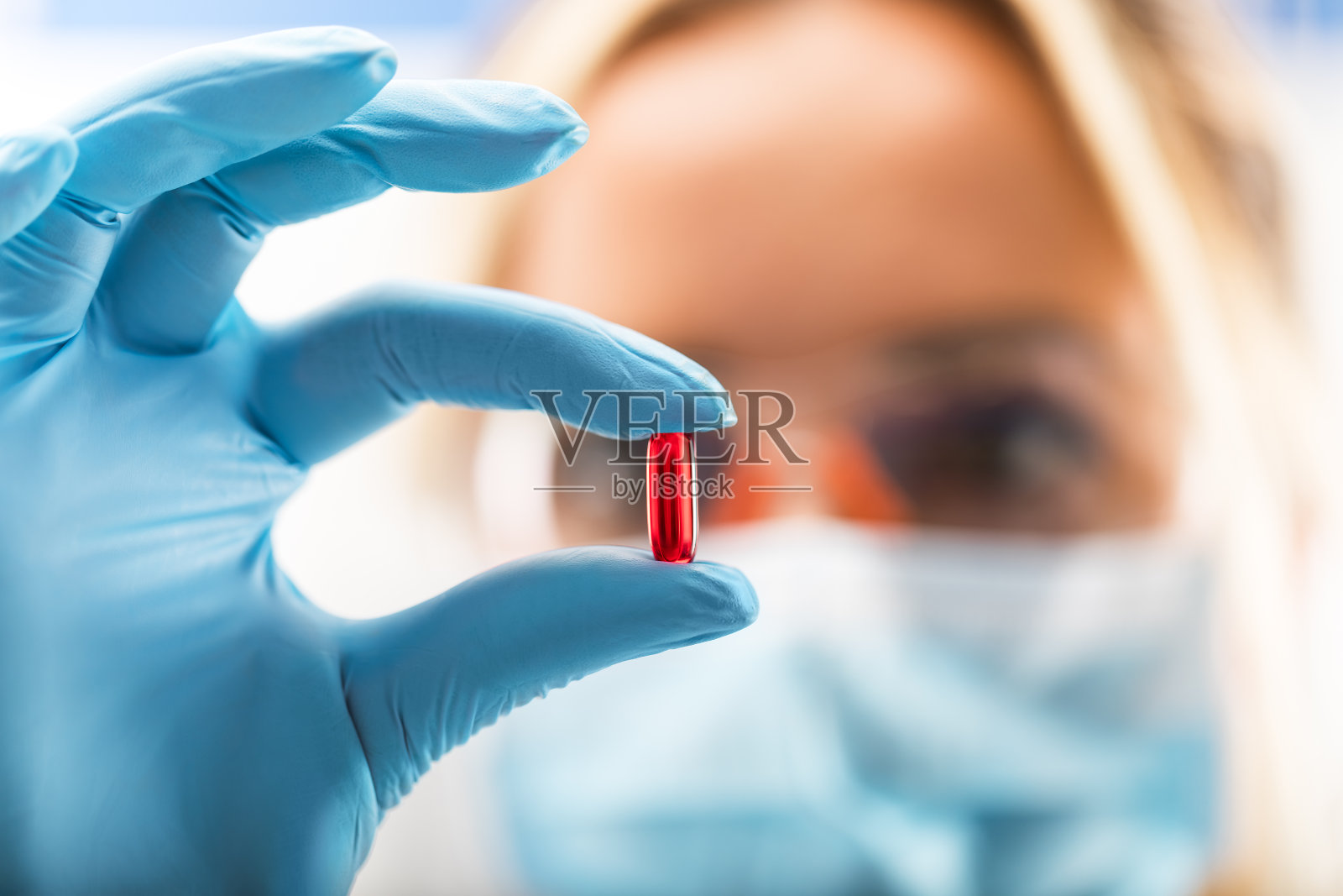 年轻迷人的女科学家拿着一颗红色透明药丸照片摄影图片