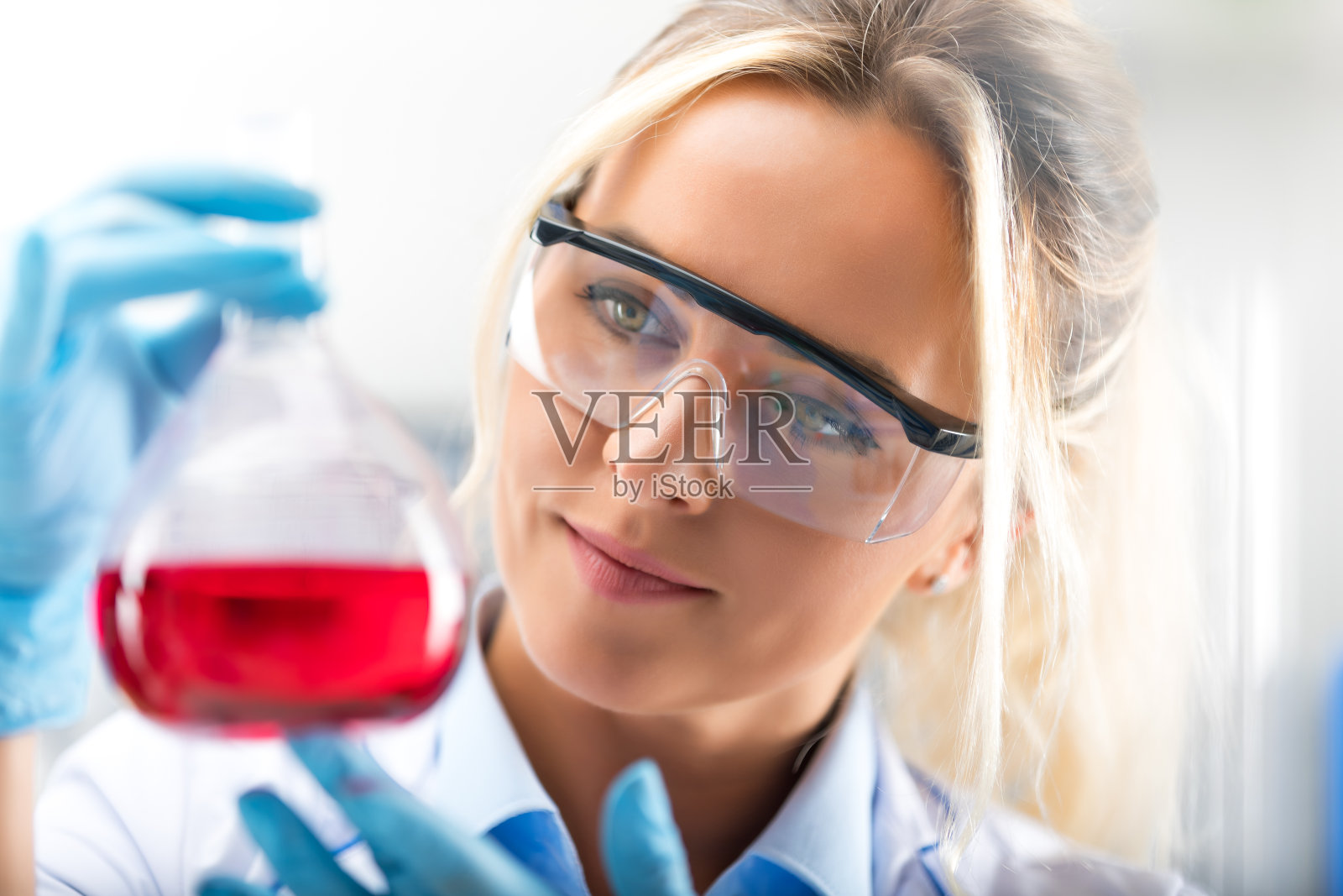 年轻迷人的女科学家拿着一个烧瓶与红色液体物质在实验室照片摄影图片