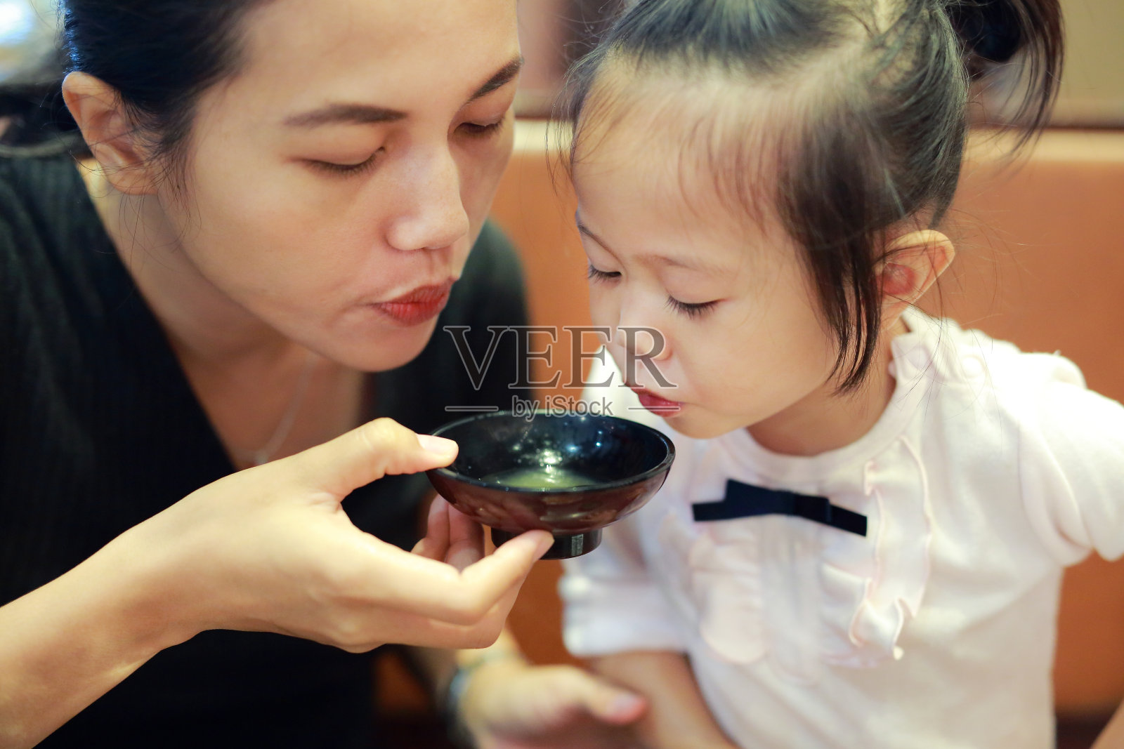 快乐的小女孩和妈妈在日本餐厅吹热味噌汤。照片摄影图片