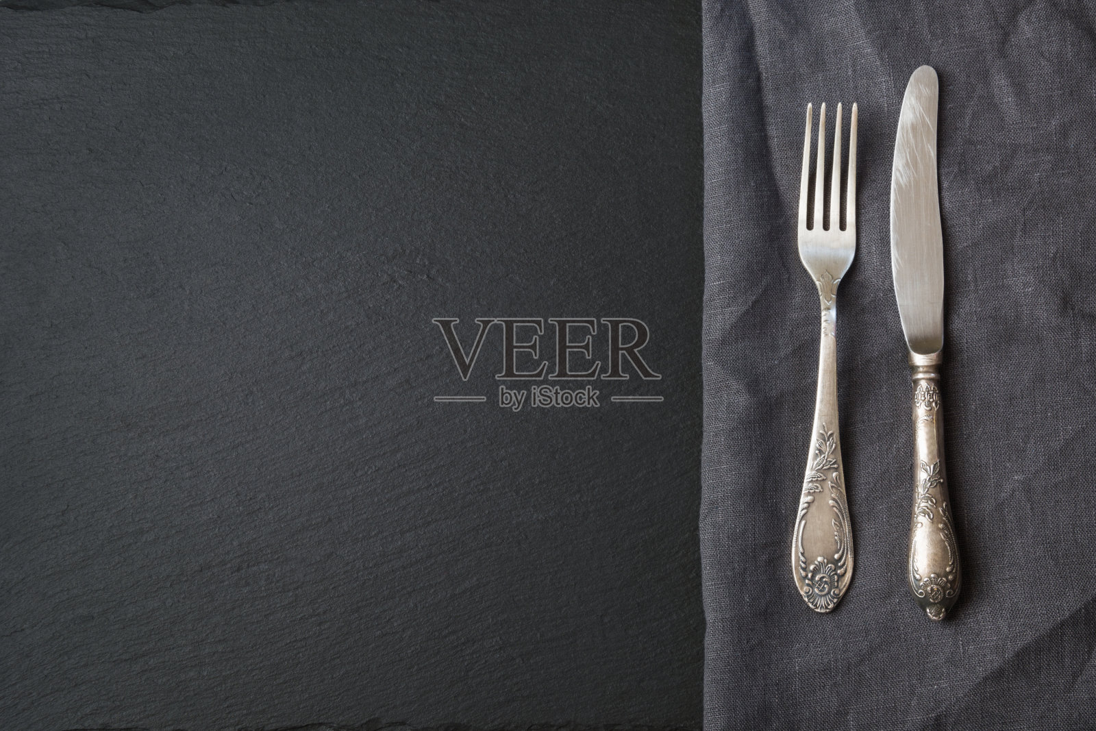 质朴的灰色亚麻布餐巾，银器和黑色石板盘子，有拷贝菜单或食谱的空间。餐厅菜单卡。前视图。照片摄影图片