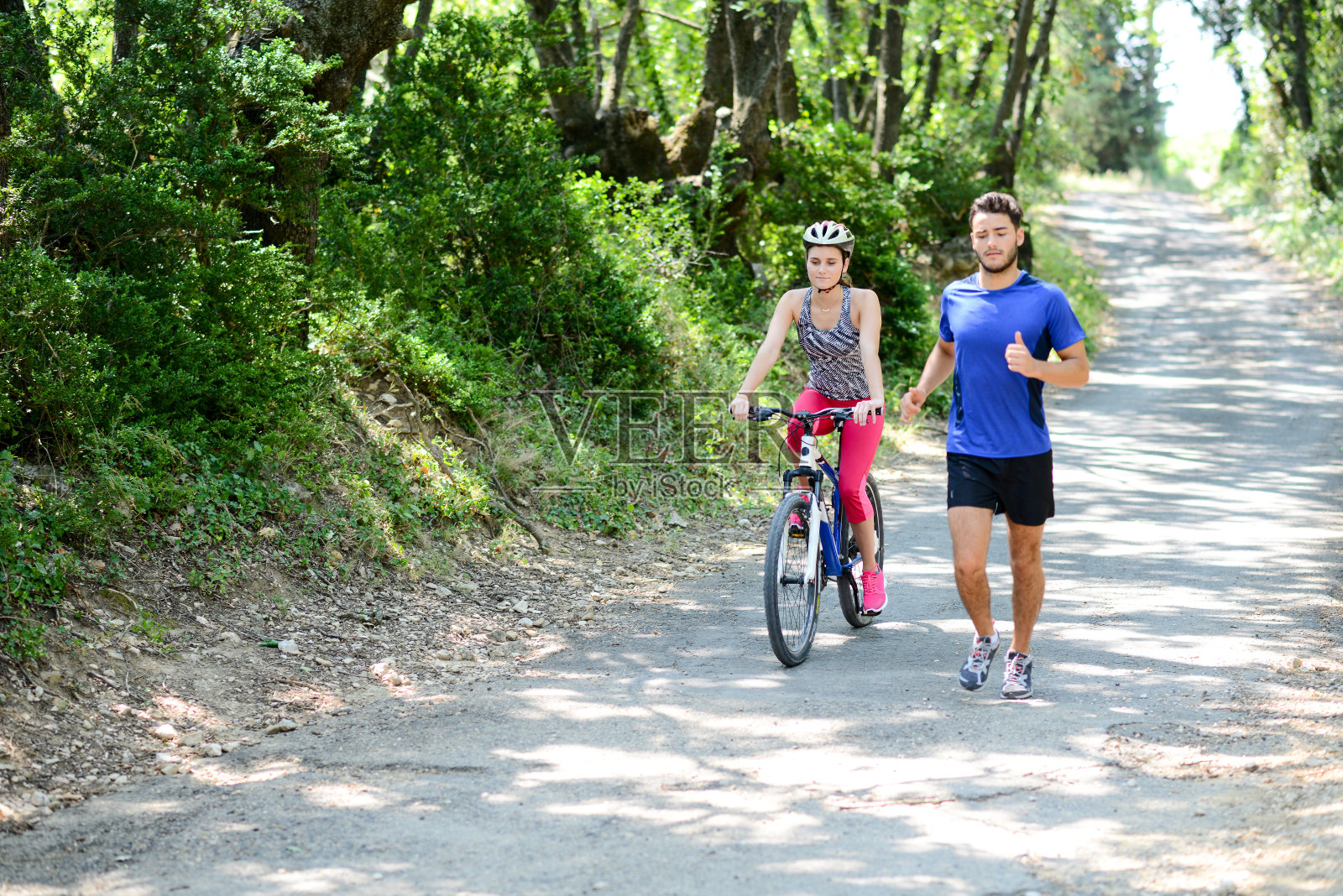 在夏天的乡村里，一个年轻女子骑着自行车，旁边是一个年轻男子在跑步照片摄影图片