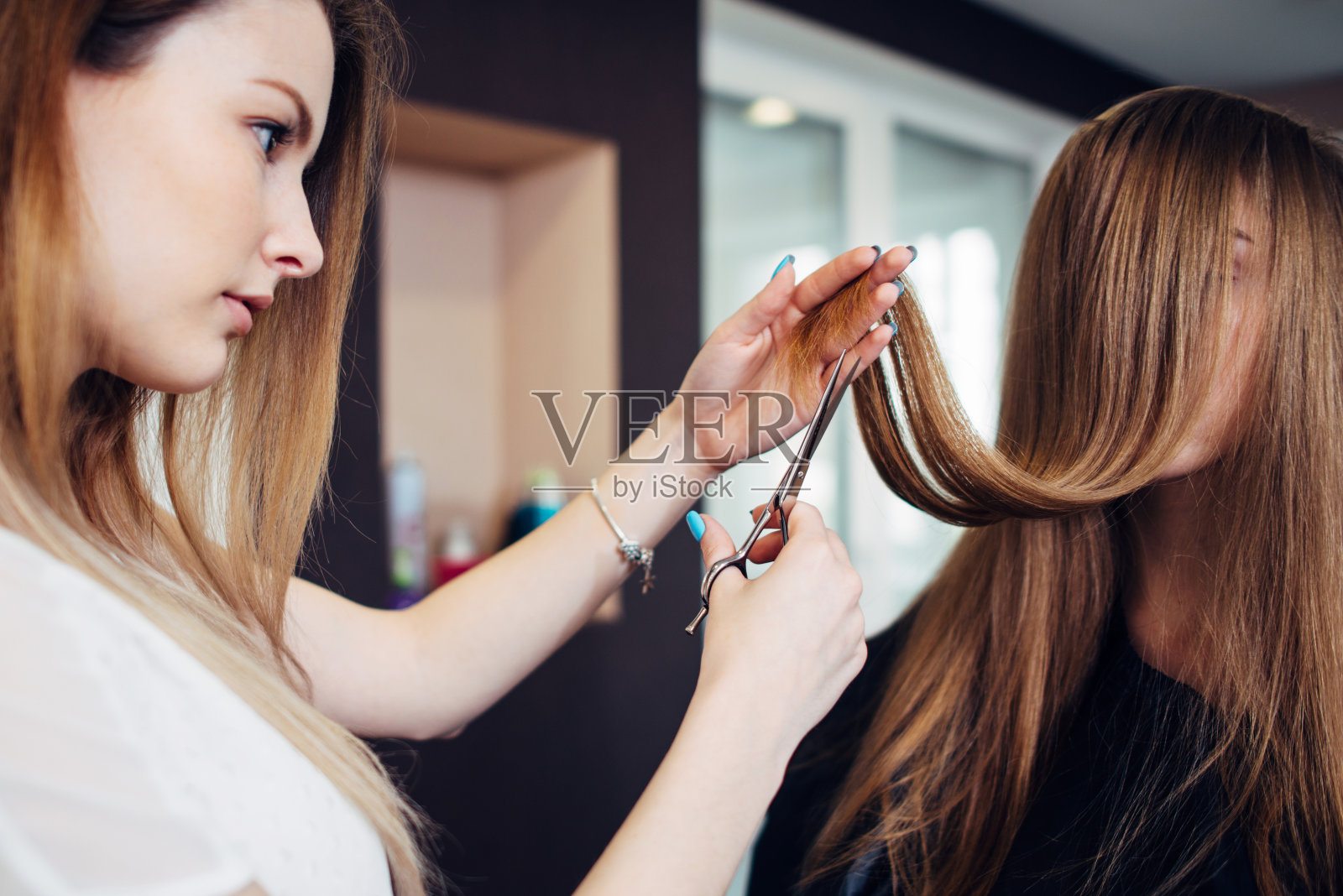 美发师为坐在美容院的长头发遮脸的女顾客修剪发梢分叉照片摄影图片