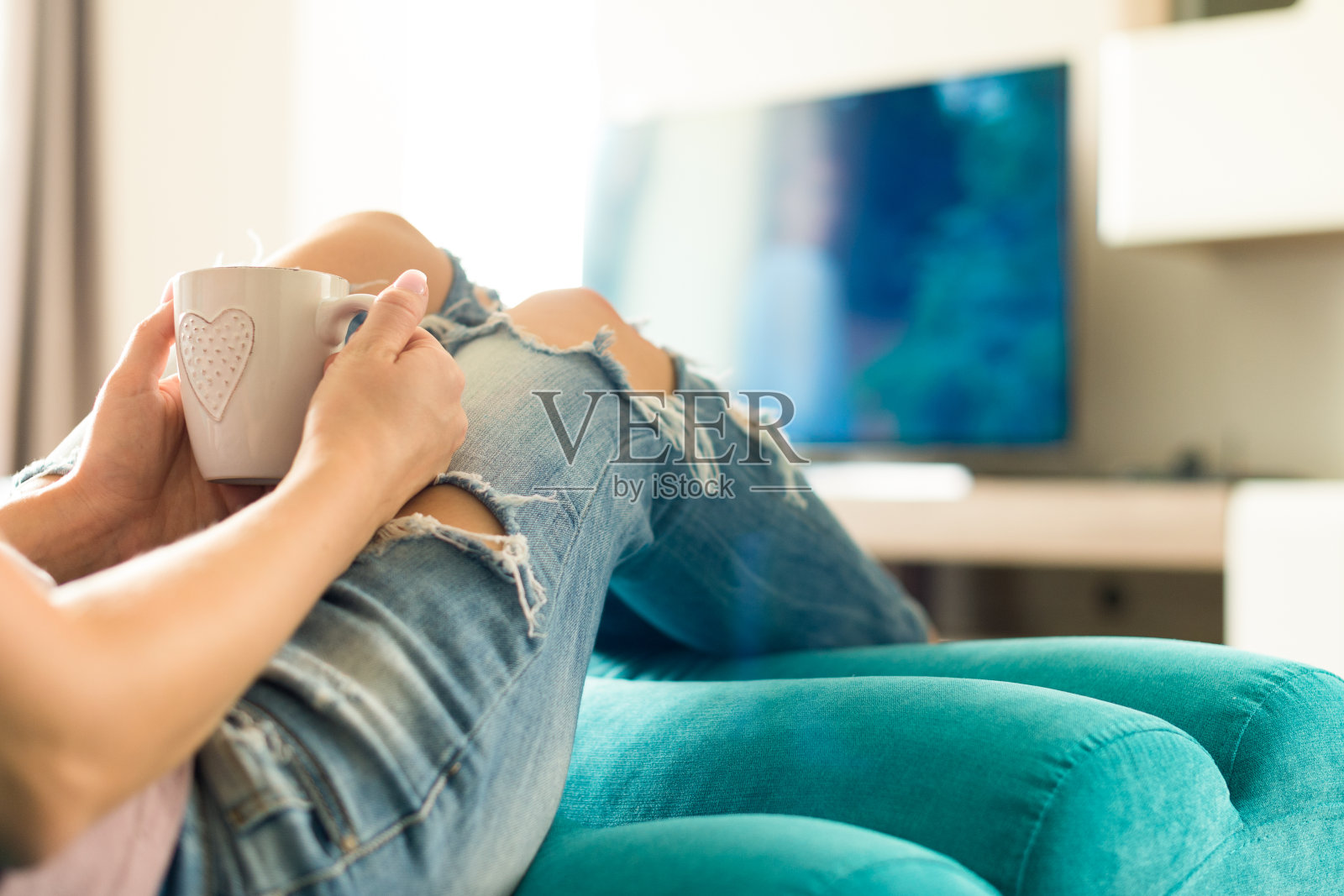 年轻女子在沙发上放松，看电视喝咖啡照片摄影图片