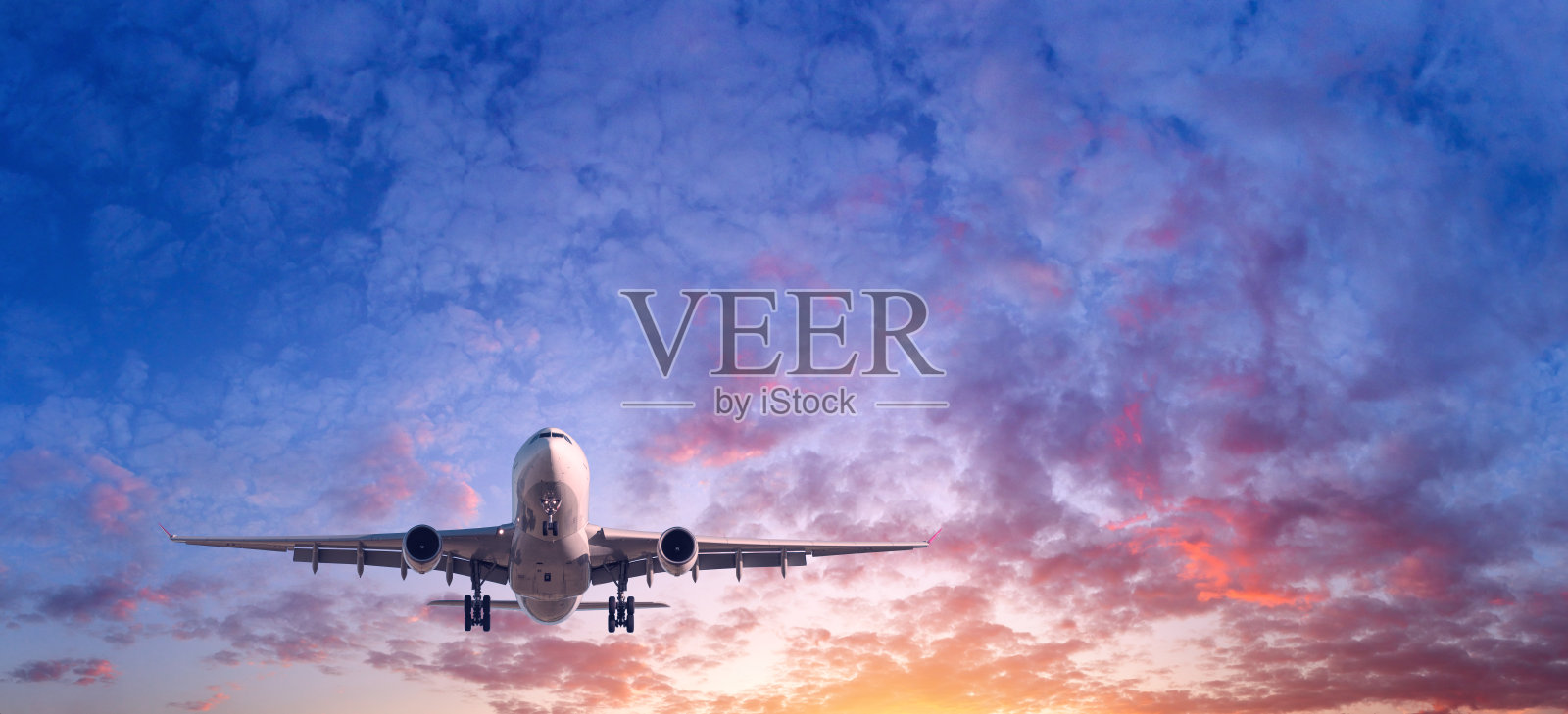 飞机着陆。落日时分，蓝天上布满了红、紫、橙三色的云雾，风景如画的客机正在飞翔。旅游的背景。客运班机。商用飞机。私人飞机照片摄影图片