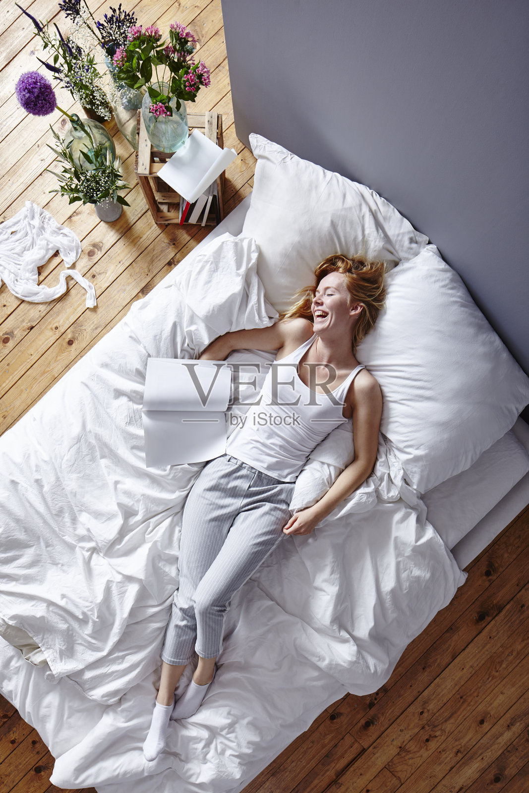 年轻迷人的红头发女人在床上看杂志和笑照片摄影图片