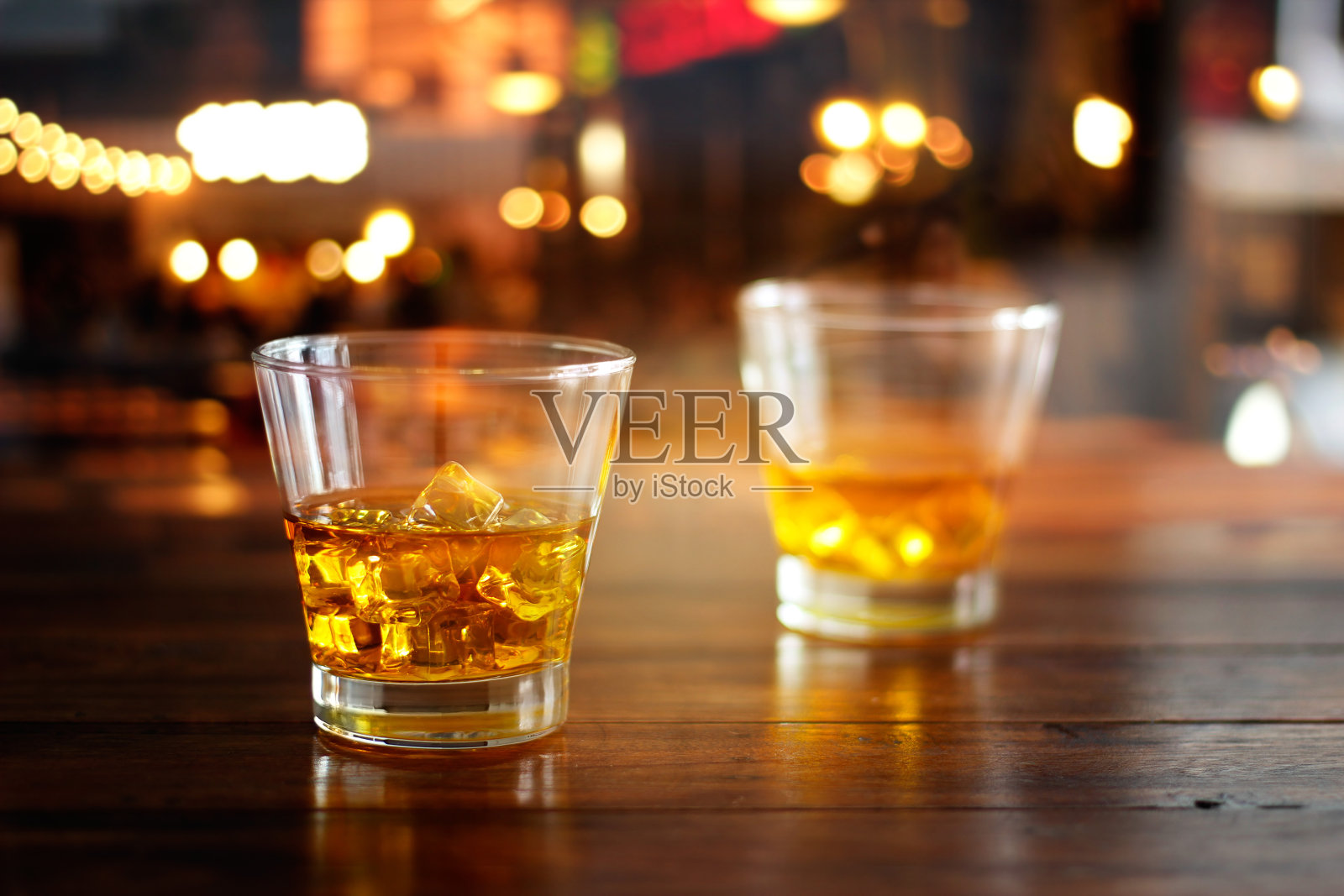 威士忌酒杯和冰块在彩色的夜晚酒吧的木桌上喝照片摄影图片