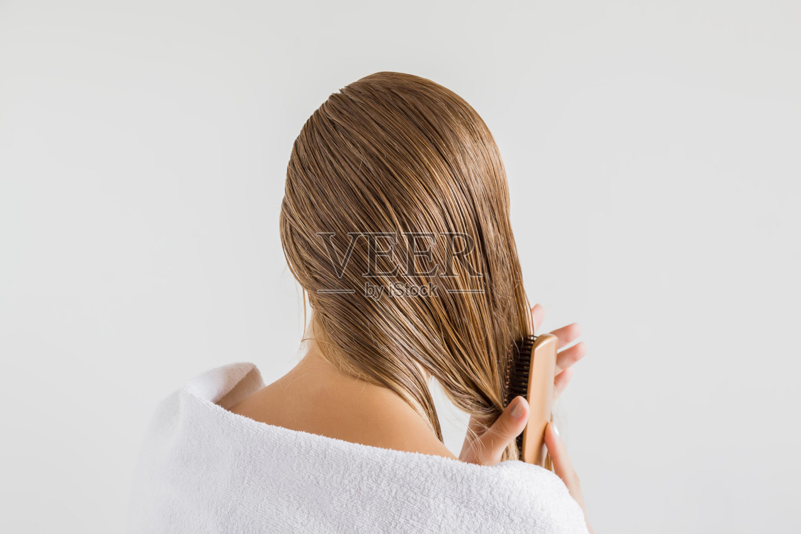 在灰色的背景下，一个女人在洗完澡后用梳子梳着她的湿金发。关心健康清洁的头发。美容院的概念。照片摄影图片