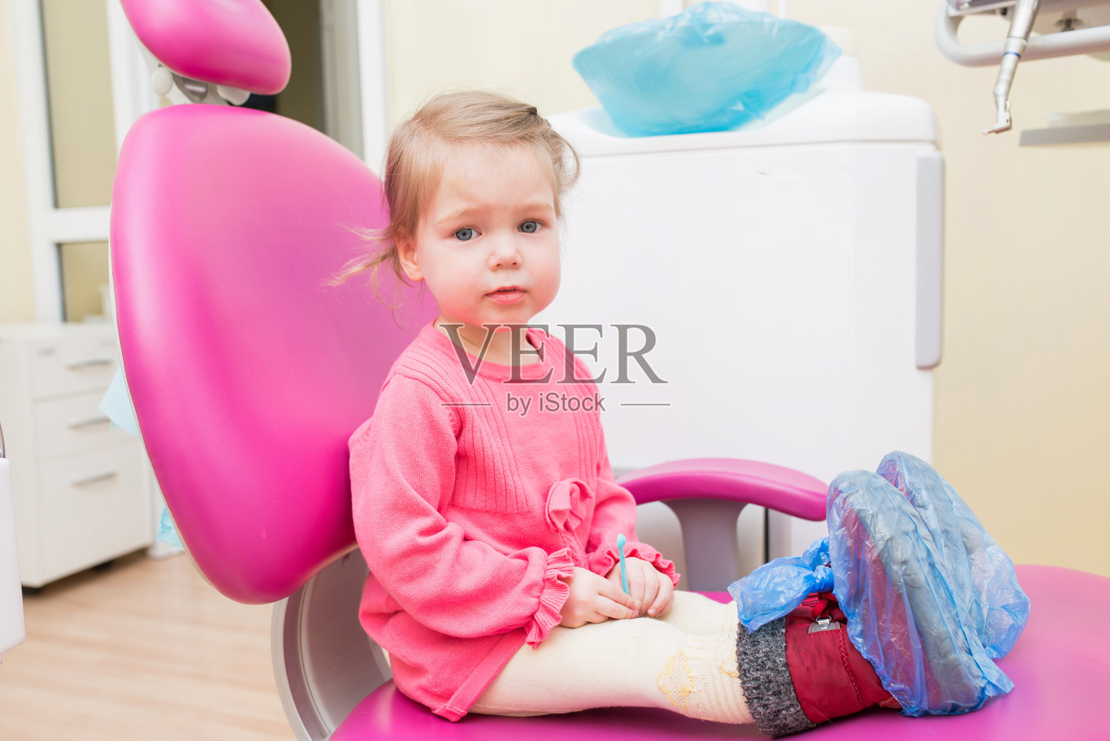 可爱的小女孩坐在牙科诊所的牙科椅上，看着镜头照片摄影图片