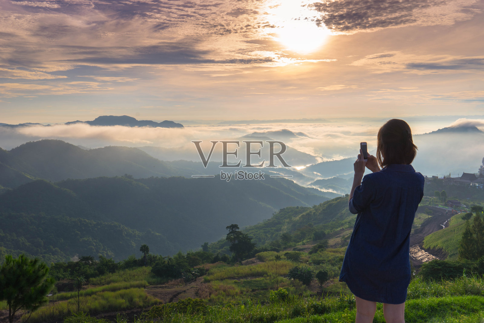 一个女人站在那里，用手机拍摄夕阳下的山脉和薄雾的全景照片摄影图片