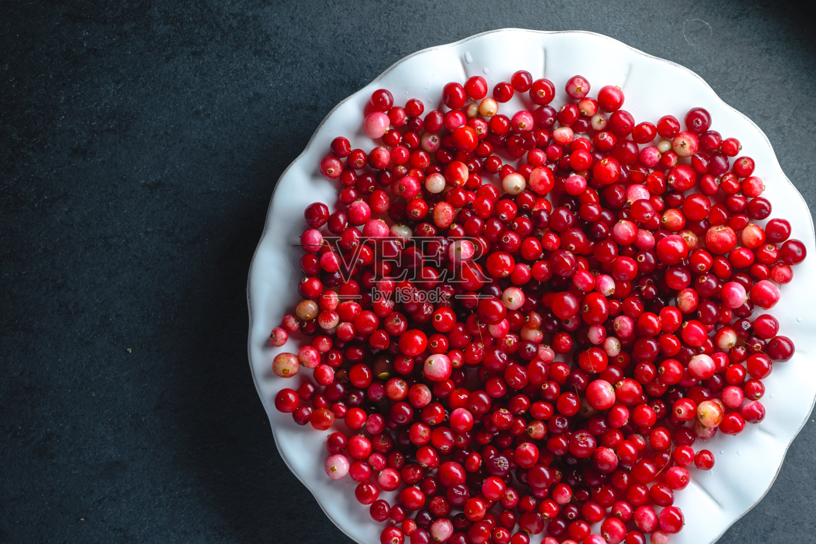 红色的蔓越莓放在一个大的白色盘子上，背景是灰色的照片摄影图片