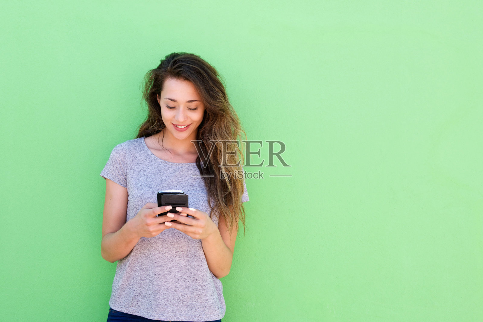 美丽的年轻女子拿着智能手机在绿色的背景照片摄影图片
