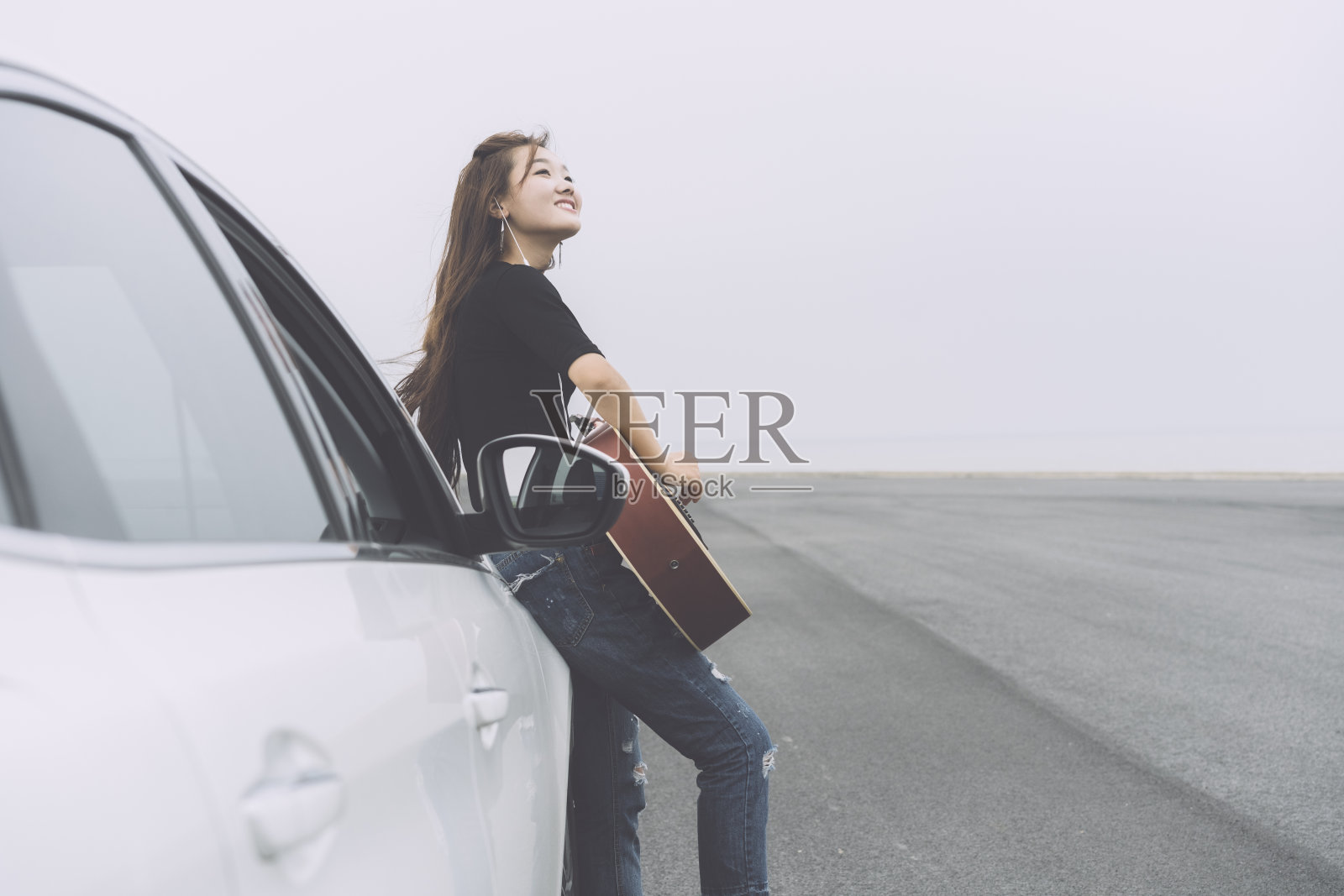 美丽的女孩听着音乐，靠在汽车引擎盖上弹吉他照片摄影图片