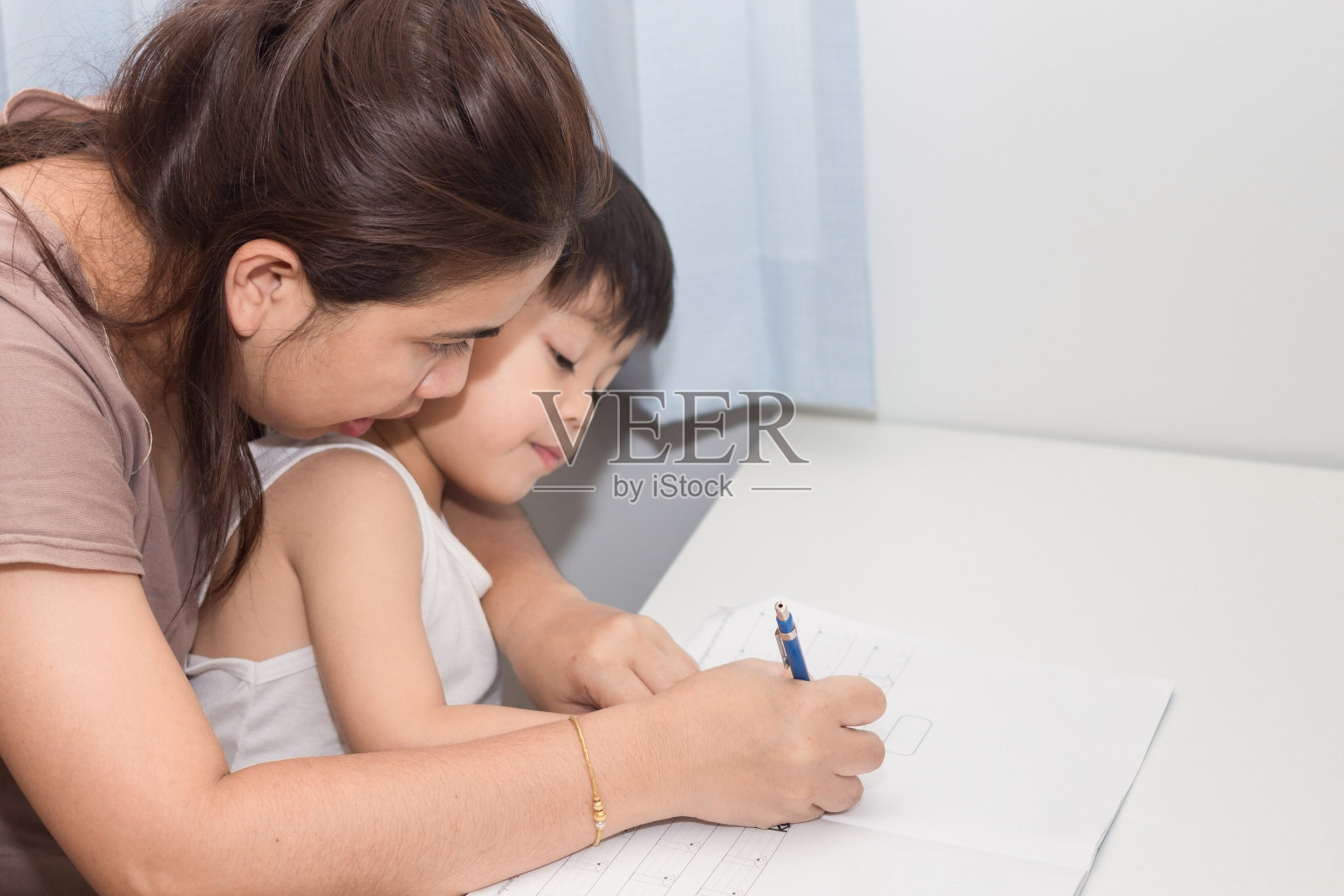 妈妈正在教儿子在纸上写字。照片摄影图片