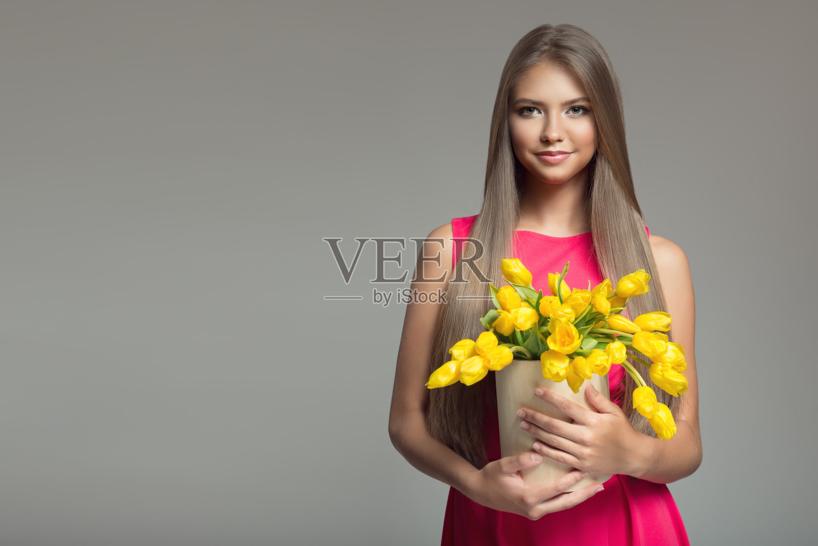 年轻快乐的女人，拿着一个装满黄色郁金香的篮子。灰色的背景。照片摄影图片