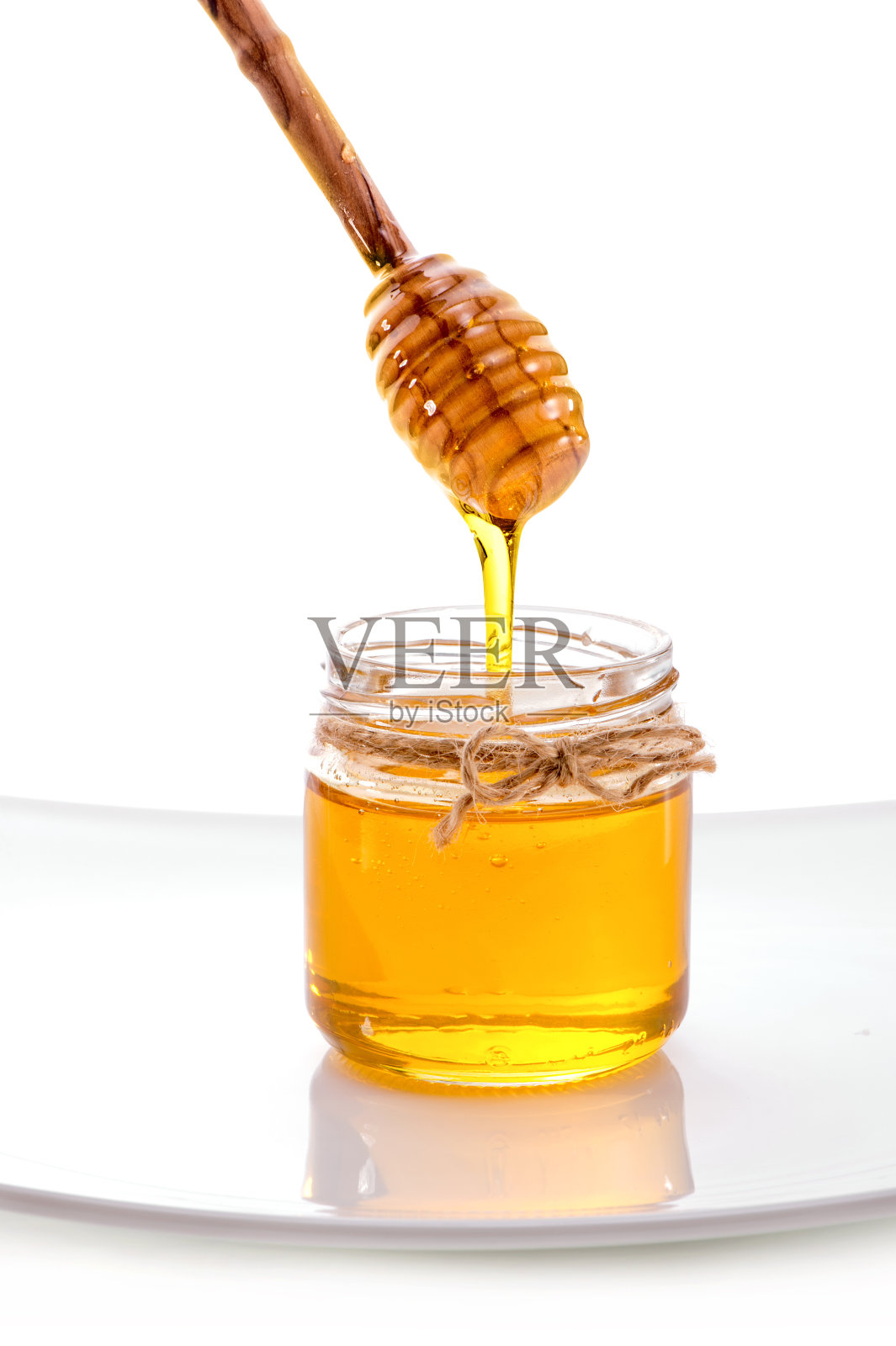 液体蜂蜜从勺子流进罐子里近距离隔离在白色的背景照片摄影图片