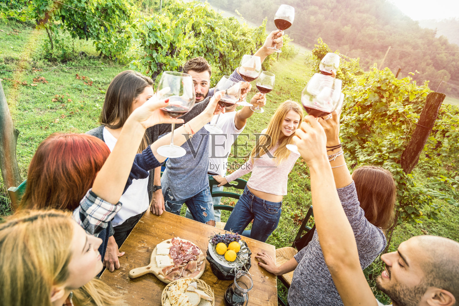 年轻的朋友们在户外喝红酒杯-快乐的人们在农家葡萄园的收获季节吃当地的食物-年轻的友谊概念在温暖的vintage过滤器照片摄影图片