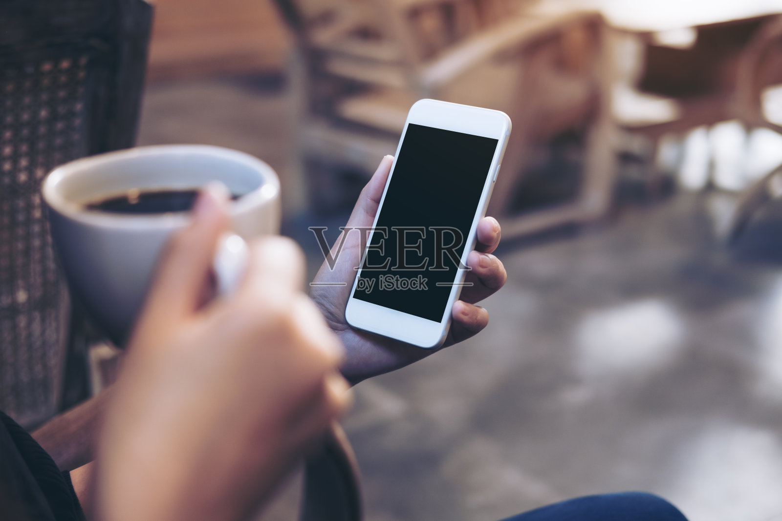 在现代阁楼咖啡馆喝咖啡的时候，女人的手拿着白色手机的黑屏模型照片摄影图片