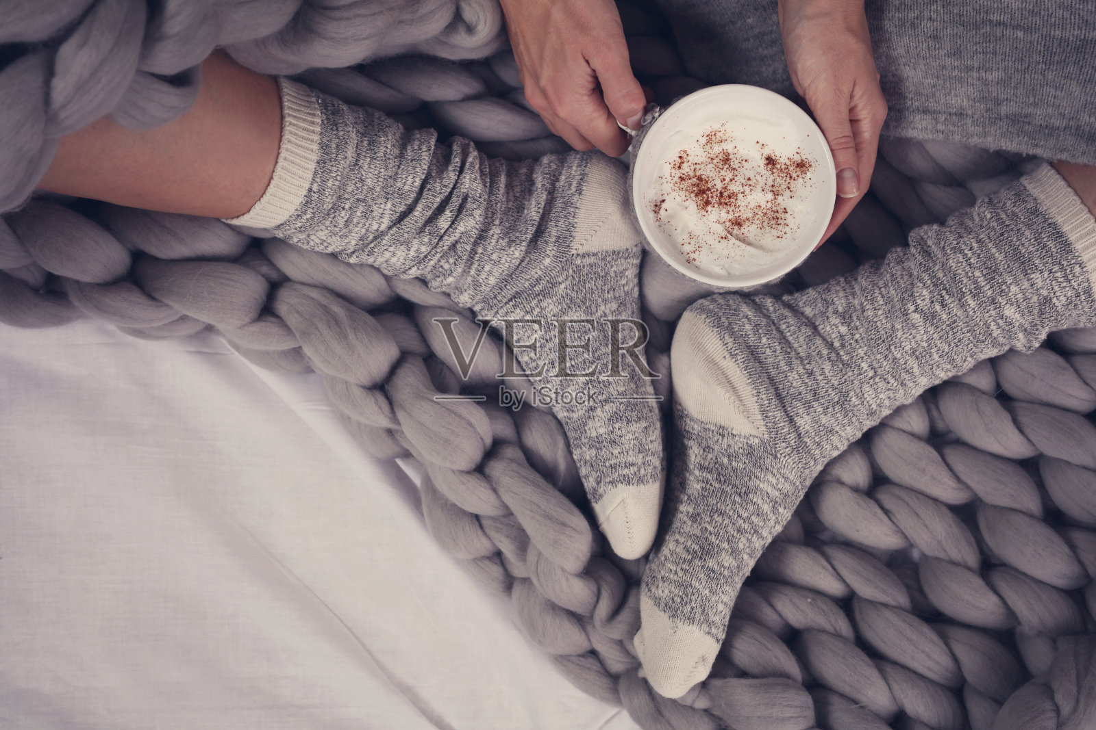 女性的脚穿着舒适温暖的羊毛袜子接近。女人盖着温暖的毯子在床上喝咖啡。照片摄影图片