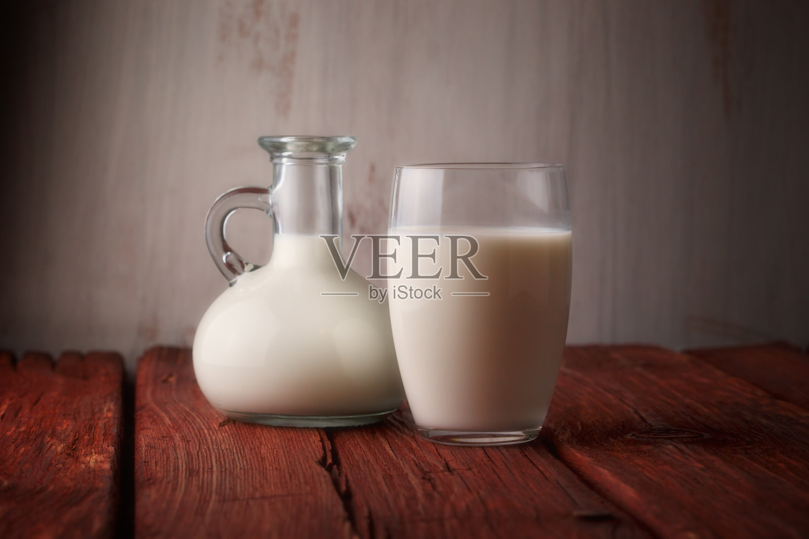 新鲜牛奶在玻璃罐和玻璃在木制背景。照片摄影图片
