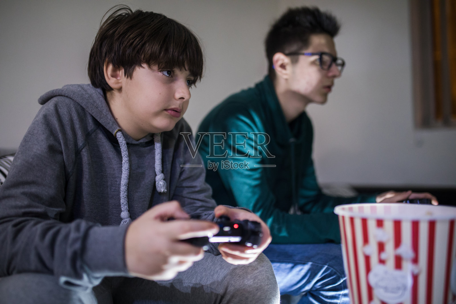 两个迷人的少年坐在家里的沙发上玩游戏机，面带微笑照片摄影图片