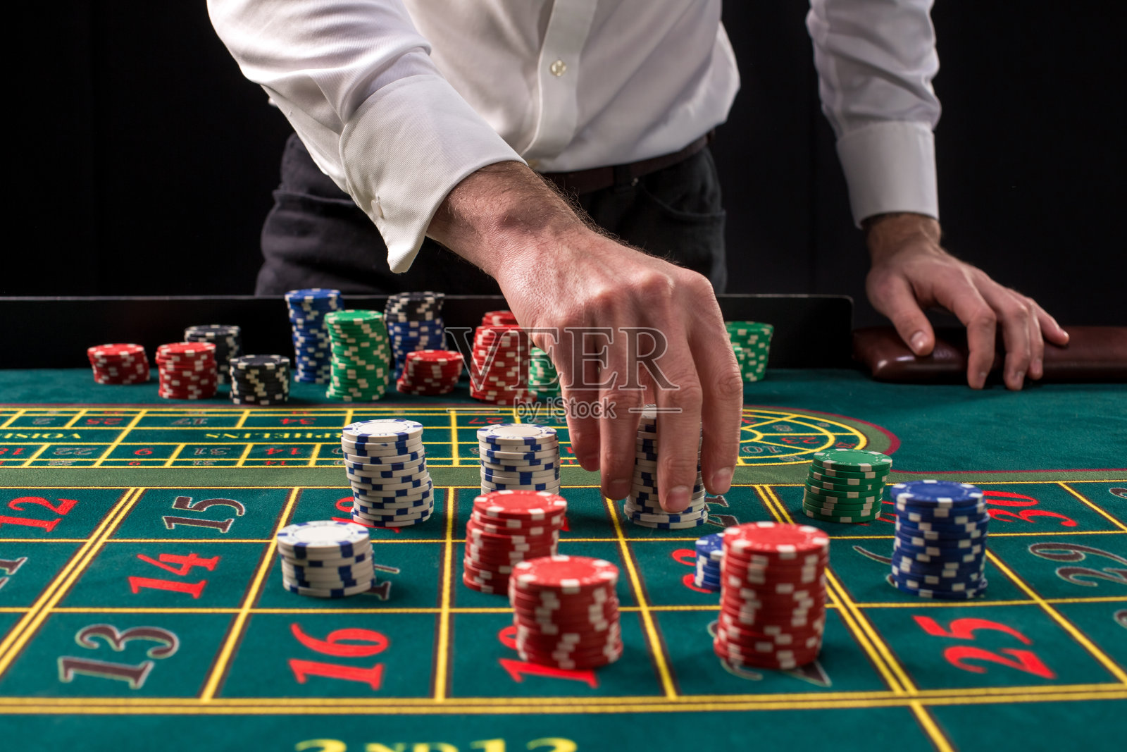 一个充满活力的绿色赌场桌子的特写图像与轮盘，与手的croupier和多色筹码照片摄影图片