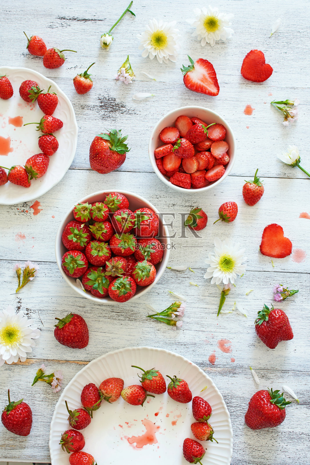 俯视图新鲜草莓在碗和盘子上装饰着花在白色的桌子。照片摄影图片