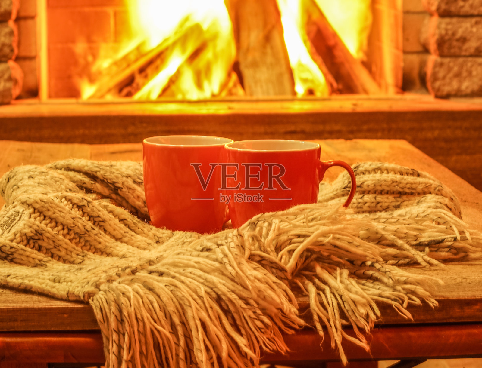 两个用来喝茶或咖啡的彩色杯子，羊毛制品放在舒适的壁炉旁。照片摄影图片