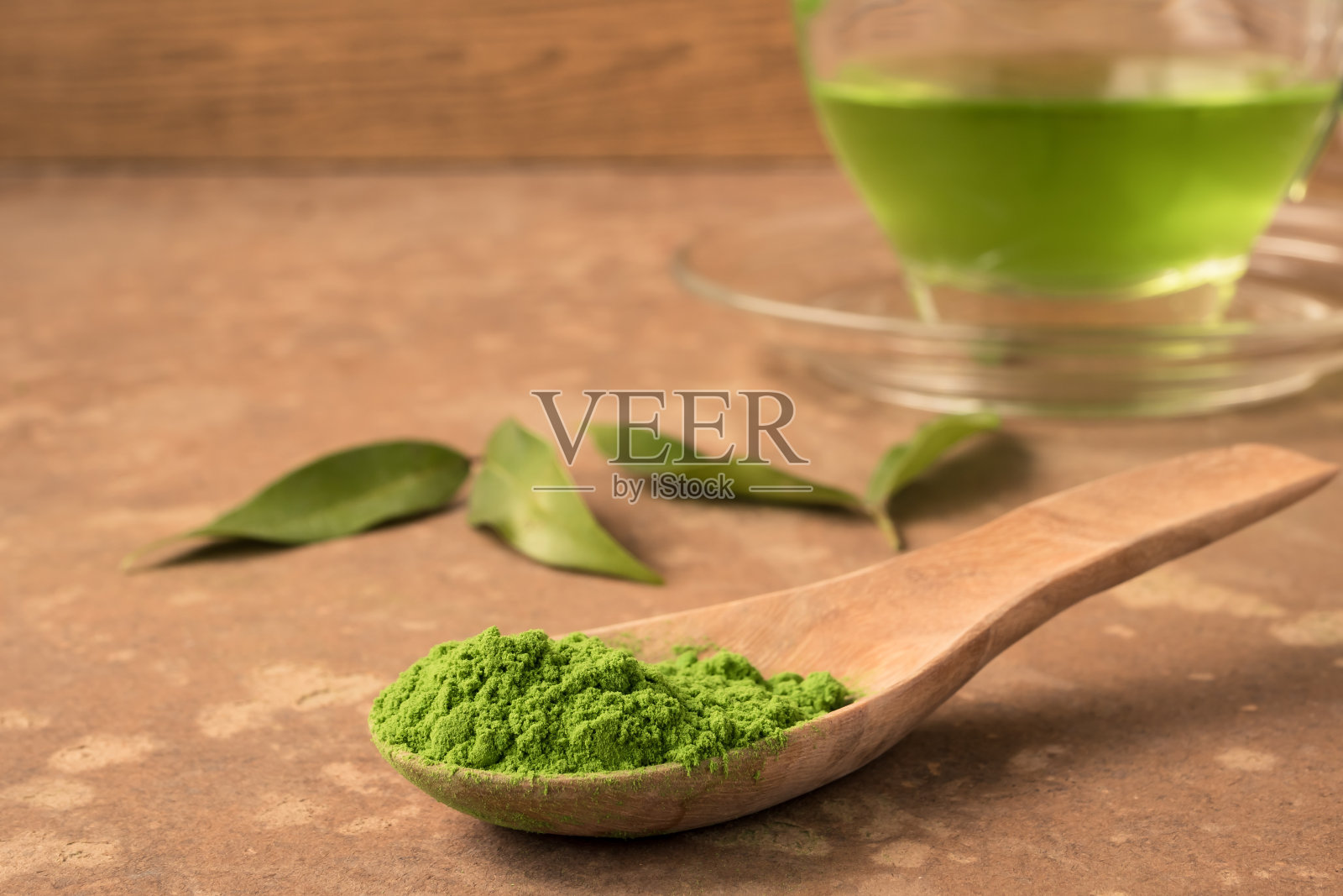 特写的绿茶粉在木勺上的桌子上与一杯热茶的背景。照片摄影图片