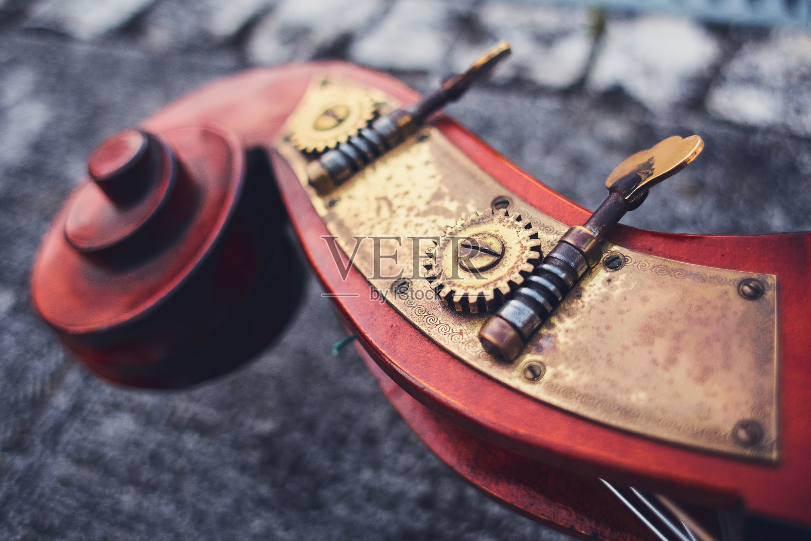 一个古老的细节大提琴的Siz红木和黄铜细节的背景上的旧铺路石。低音的木制部分，微距镜头。乐器上的青铜黄铜螺栓和齿轮。照片摄影图片