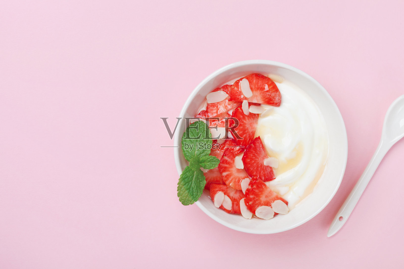 粉红色的桌子上放着一碗希腊酸奶、草莓和蜂蜜。照片摄影图片