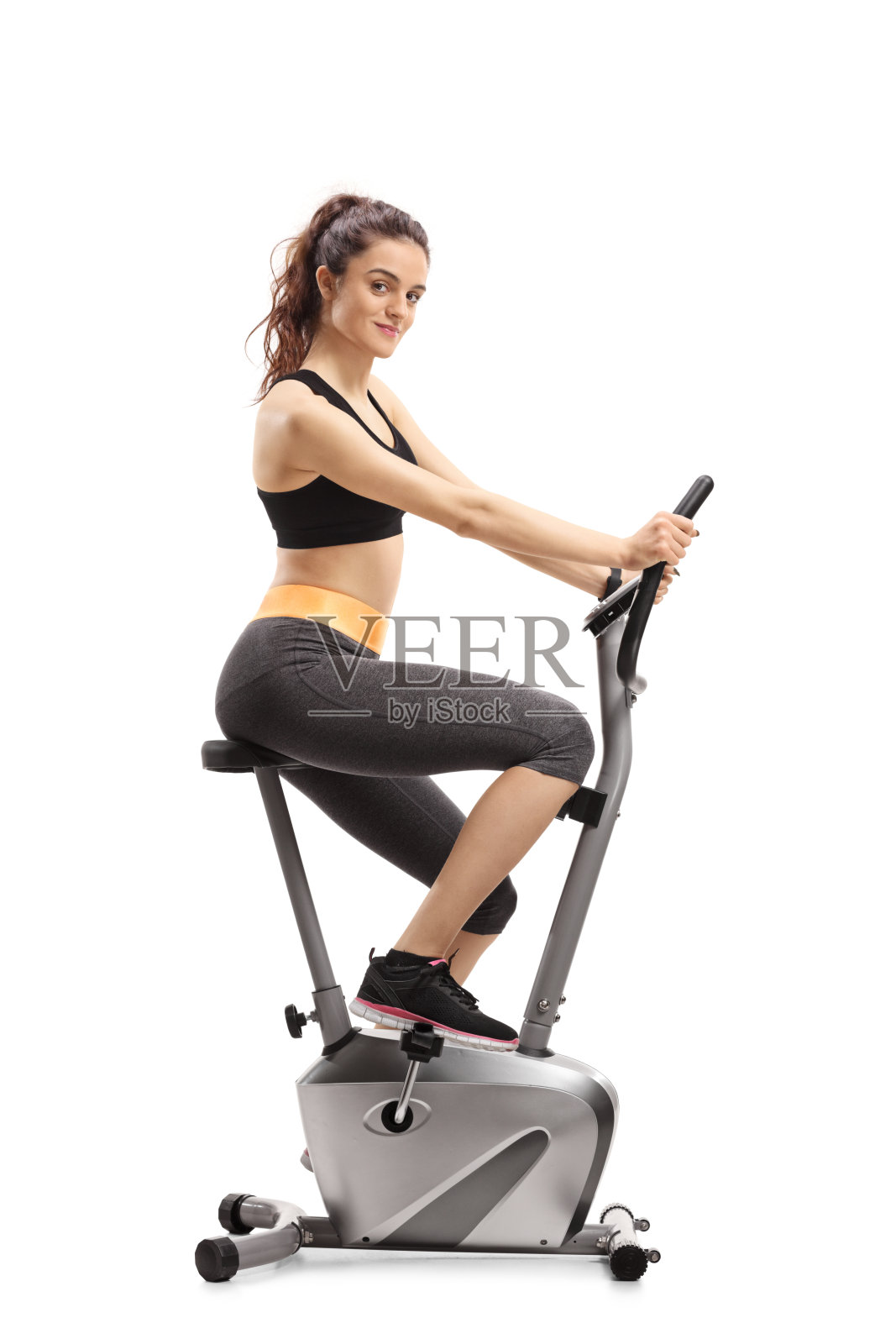 健身女性骑着健身自行车，看着镜头照片摄影图片