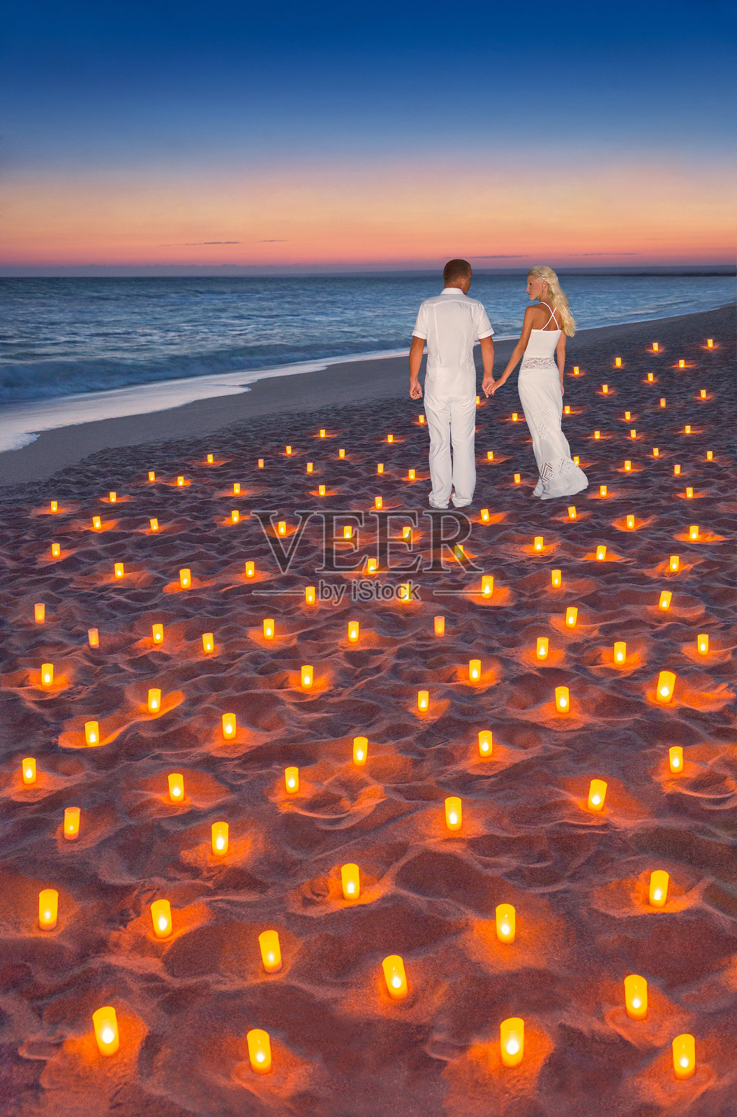 情侣在热带日落海洋沙滩和许多蜡烛。求婚、婚礼、情人节或蜜月垂直背景概念。照片摄影图片