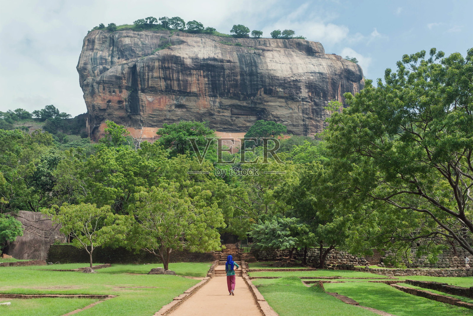 孤独的妇女戴着头巾走到著名的地标西格里亚岩石周围的绿树森林，斯里兰卡。联合国教科文组织世界遗产照片摄影图片