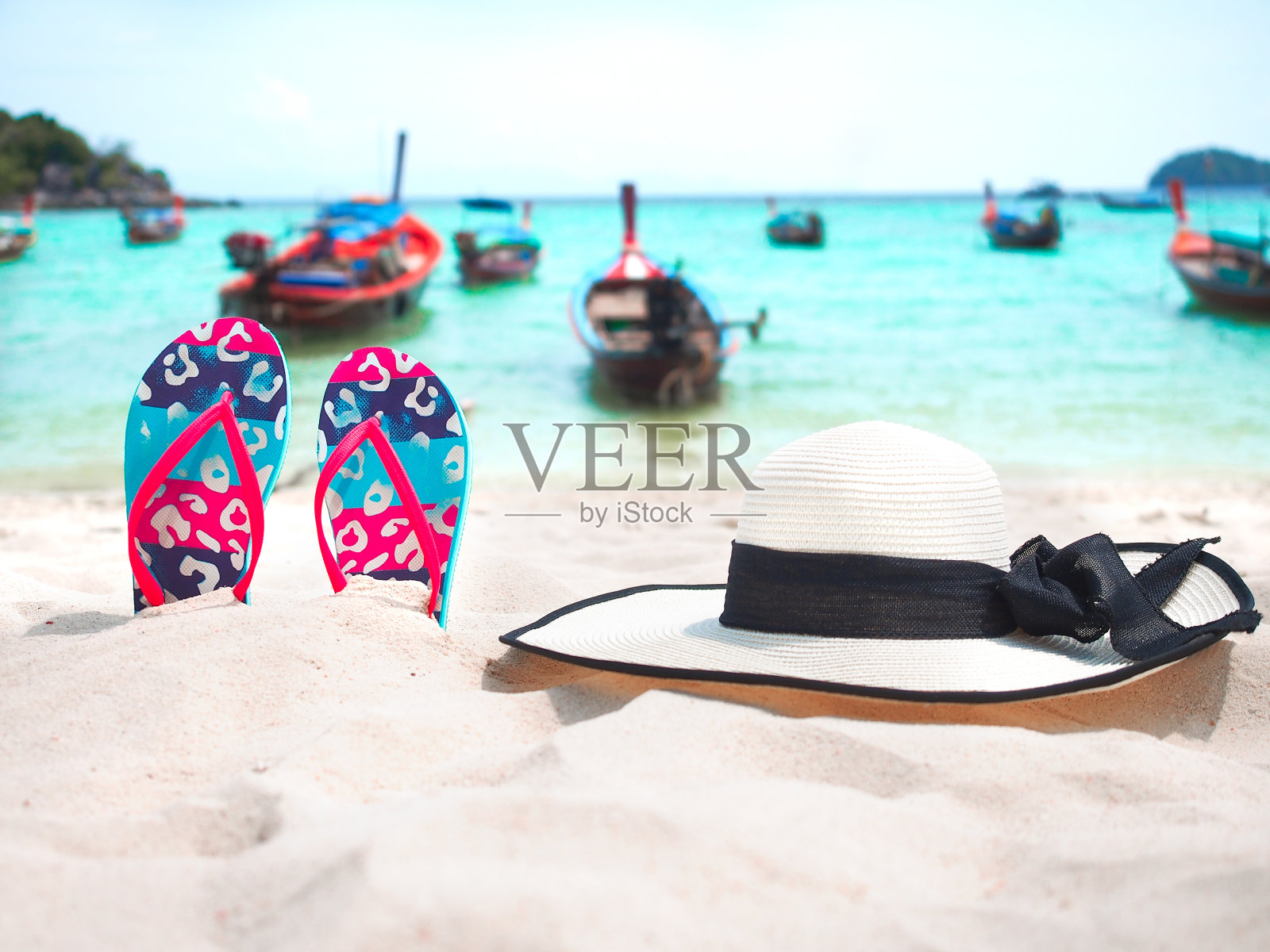 沙滩上五颜六色的人字拖和白色的帽子。照片摄影图片