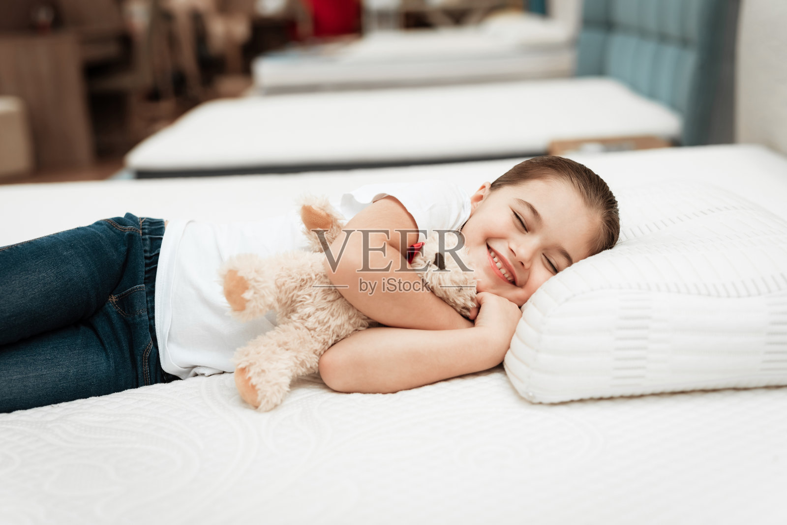一个微笑的小女孩躺在一个家具店整形床垫上。照片摄影图片